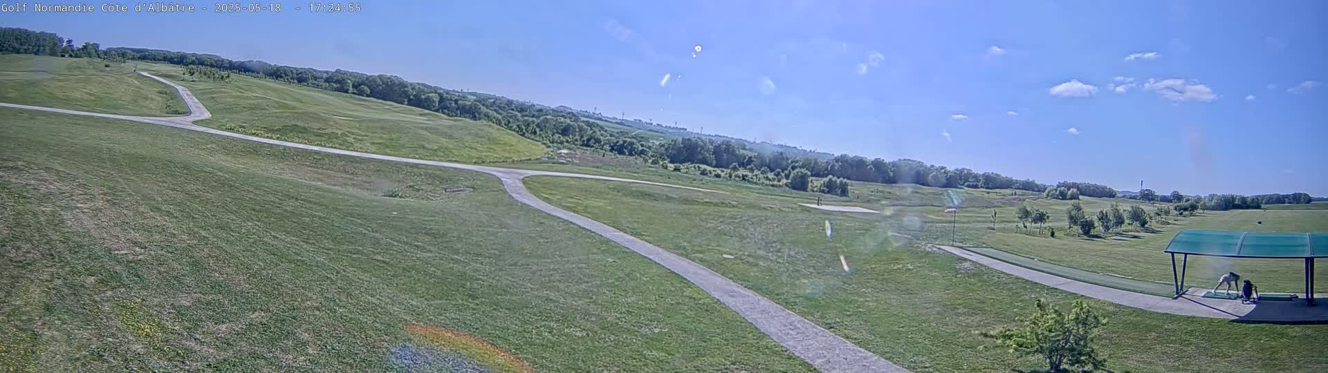 A golf course with paved paths under a mostly clear, sunny sky.