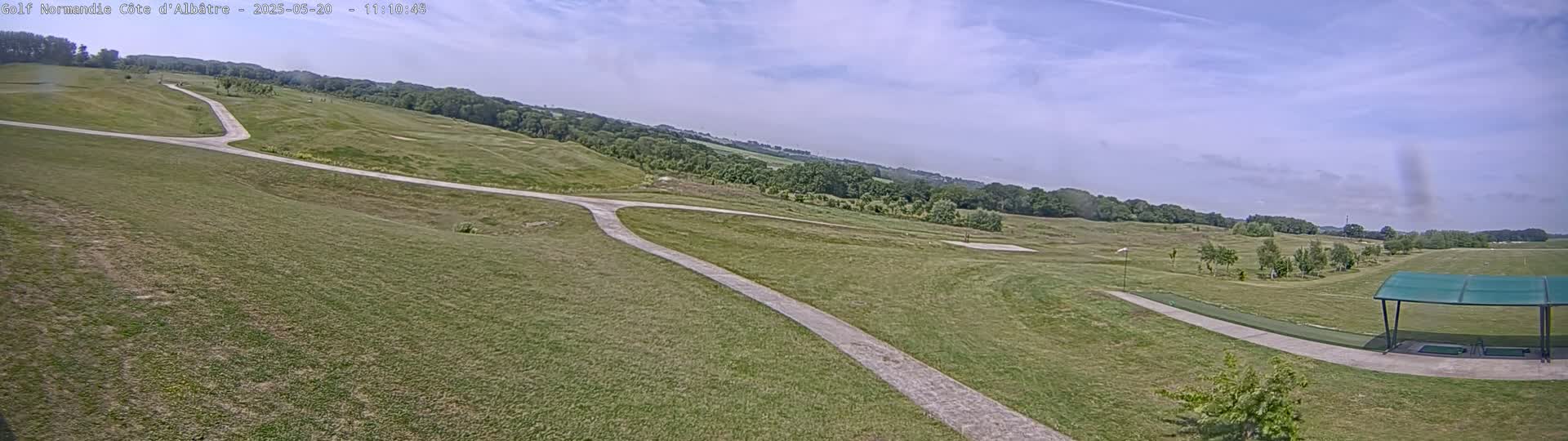 A grassy golf course with a paved path under a mostly sunny sky.