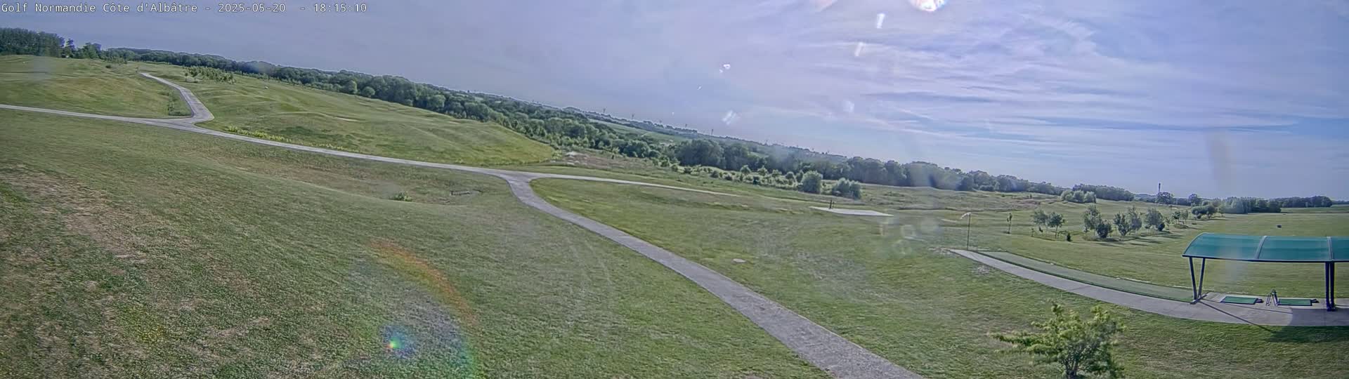 A partly sunny day reveals a sprawling golf course with winding paths and a covered driving range, surrounded by lush green fairways and trees.