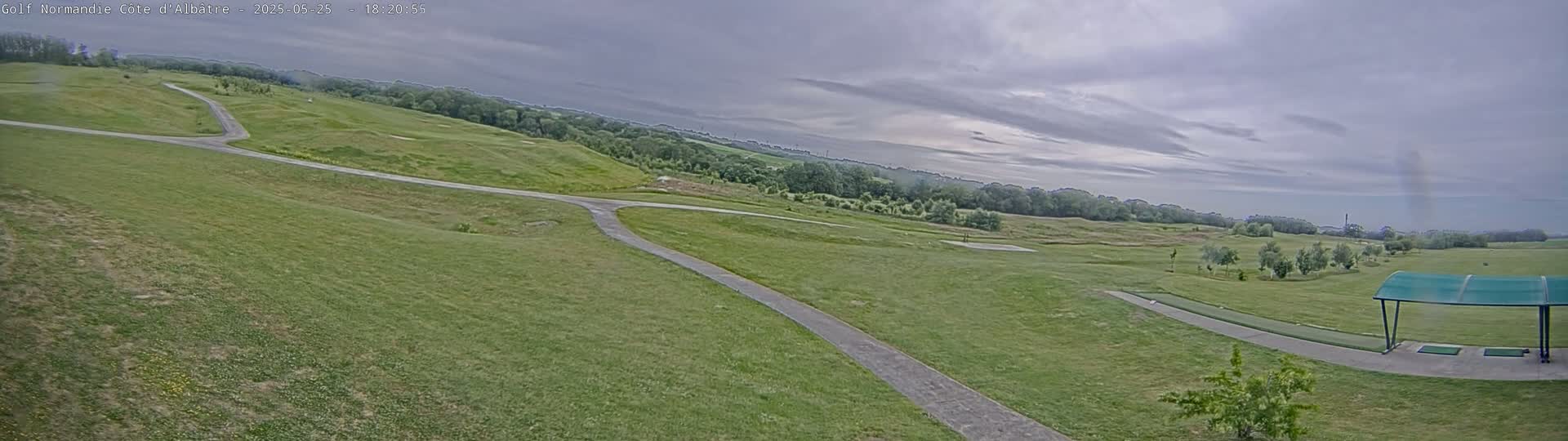 A golf course with paved pathways under a cloudy sky.