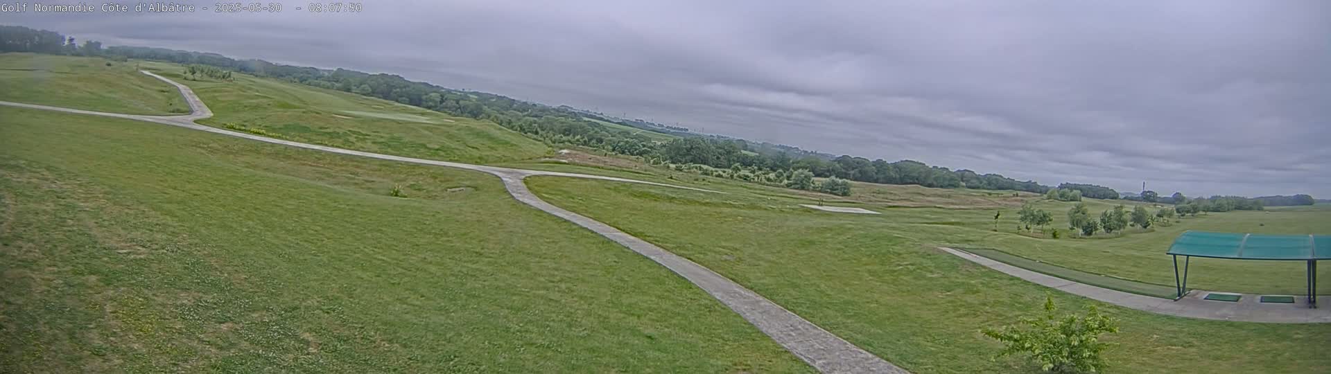 A paved path winds through a grassy golf course under a cloudy sky.