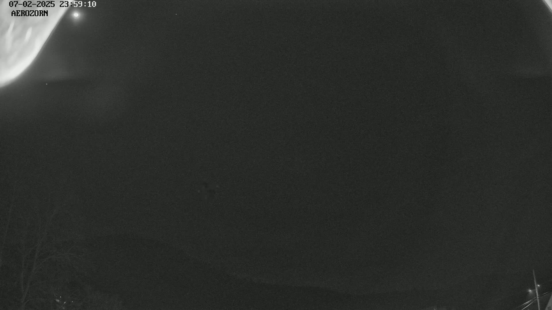 A nighttime, low-light image shows a dark sky with faint aurora borealis visible in the upper left corner, and a dark landscape below.