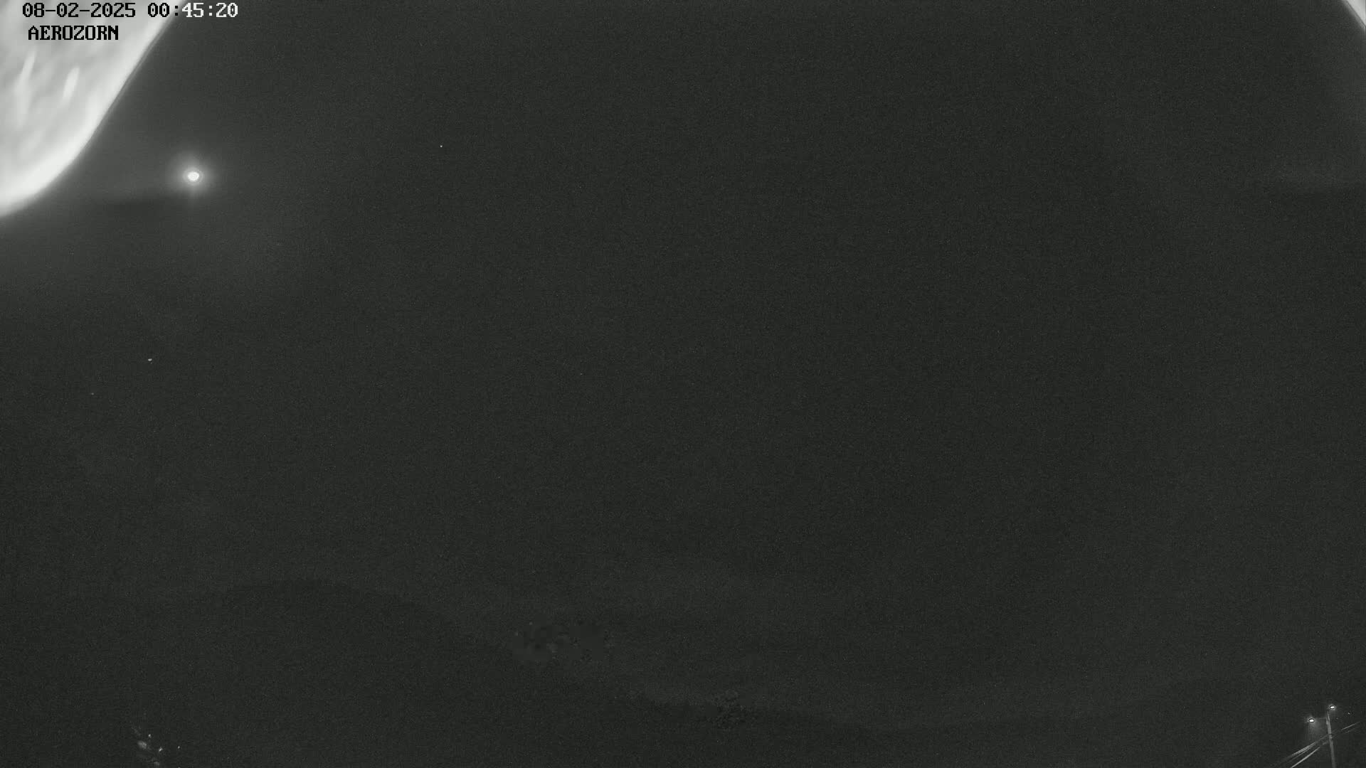 A nighttime long-exposure shot shows a dark sky with faint auroras and a bright light source, possibly the moon, visible.
