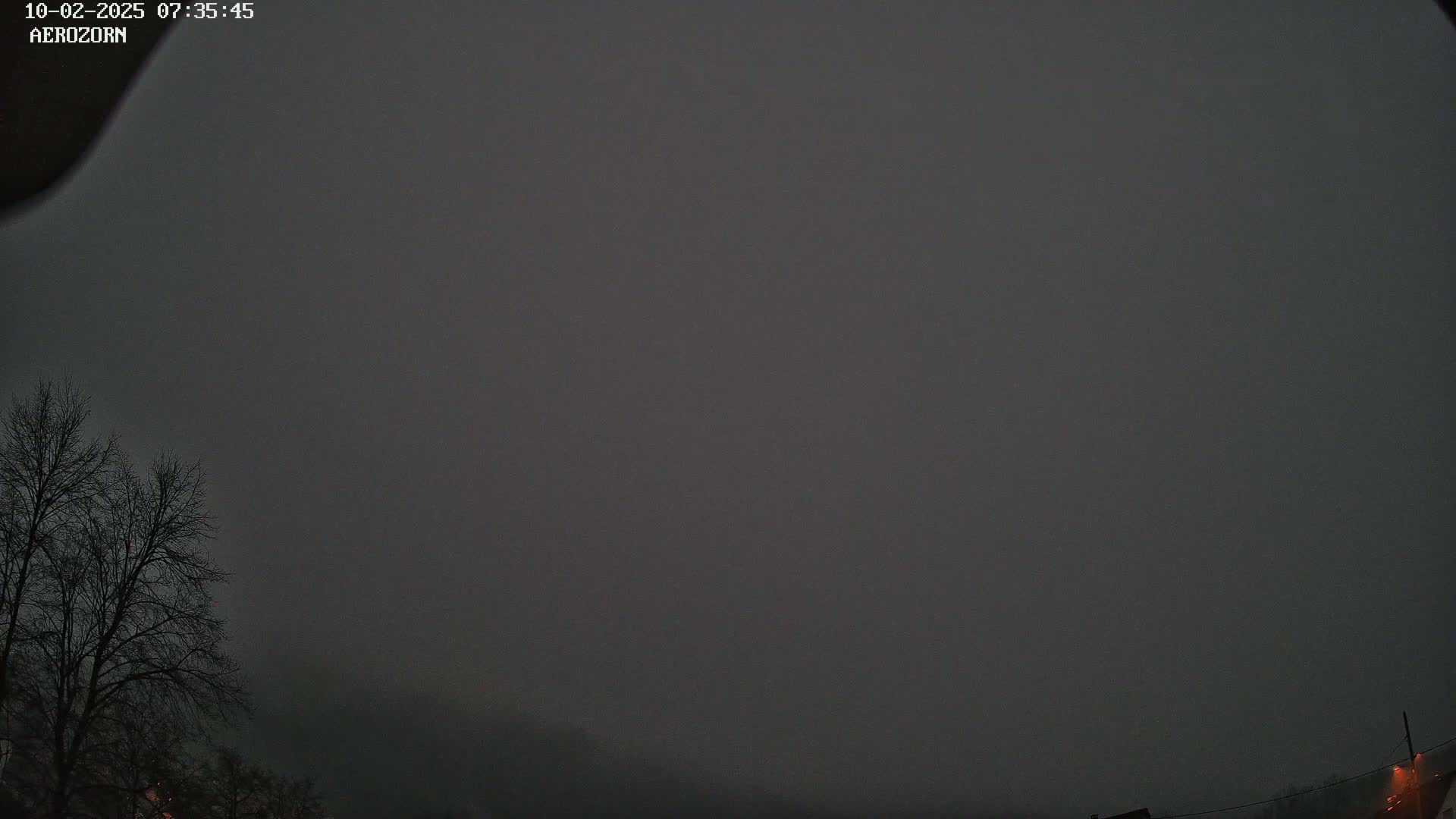A dark, overcast sky hangs over bare trees and the tops of buildings in the foggy distance.