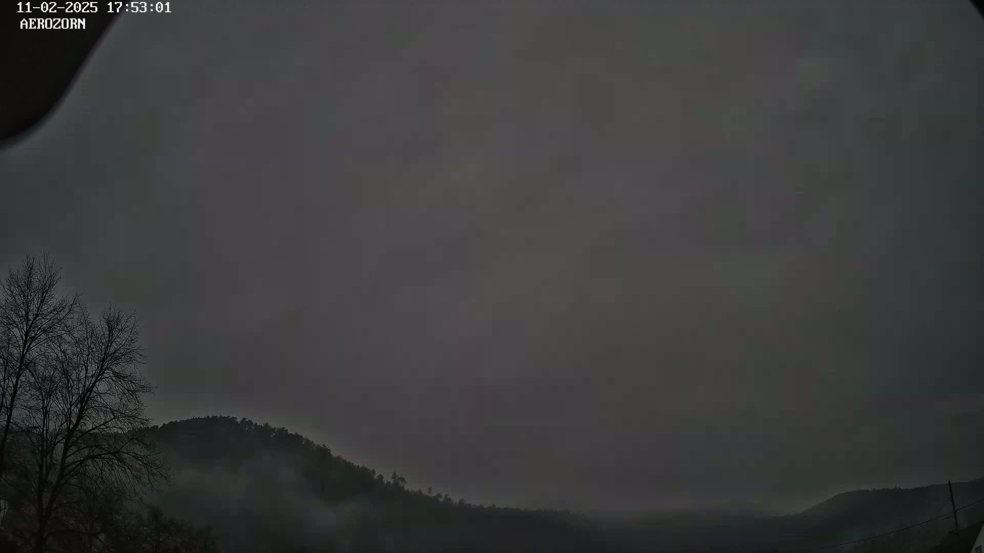 A dark, overcast sky hangs over a low-lying, fog-covered landscape of trees and hills.