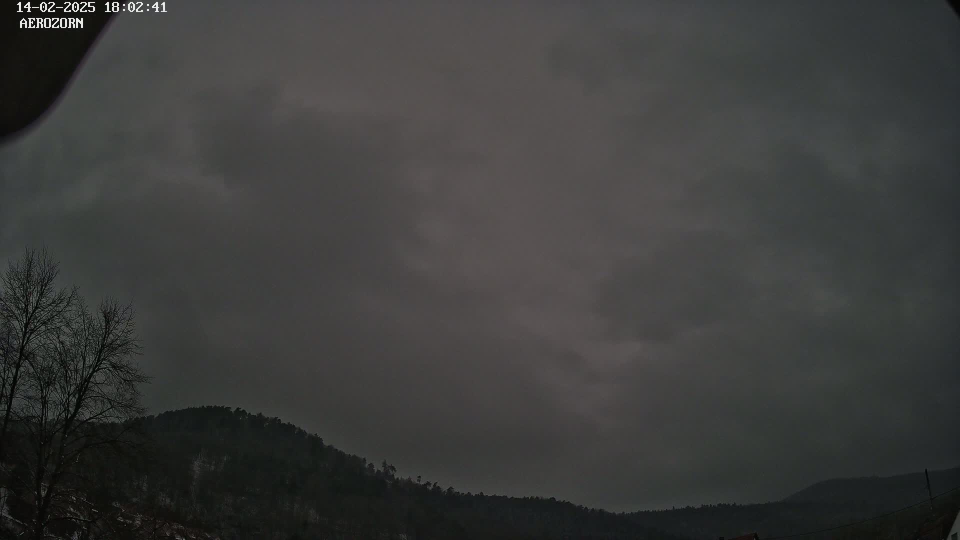 A dark, overcast sky hangs above a line of silhouetted hills and leafless trees.