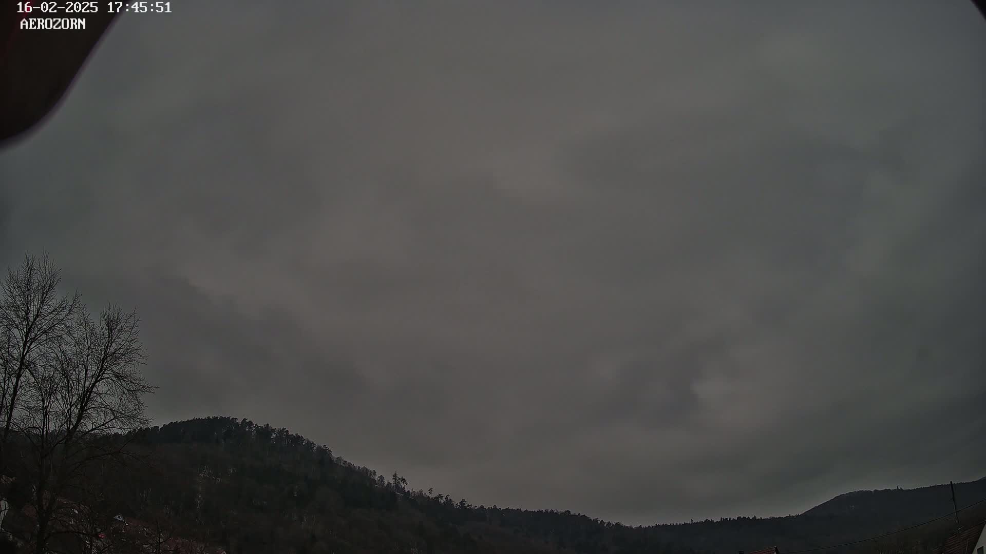 A mostly cloudy, overcast sky hangs over a dark, forested hillside.