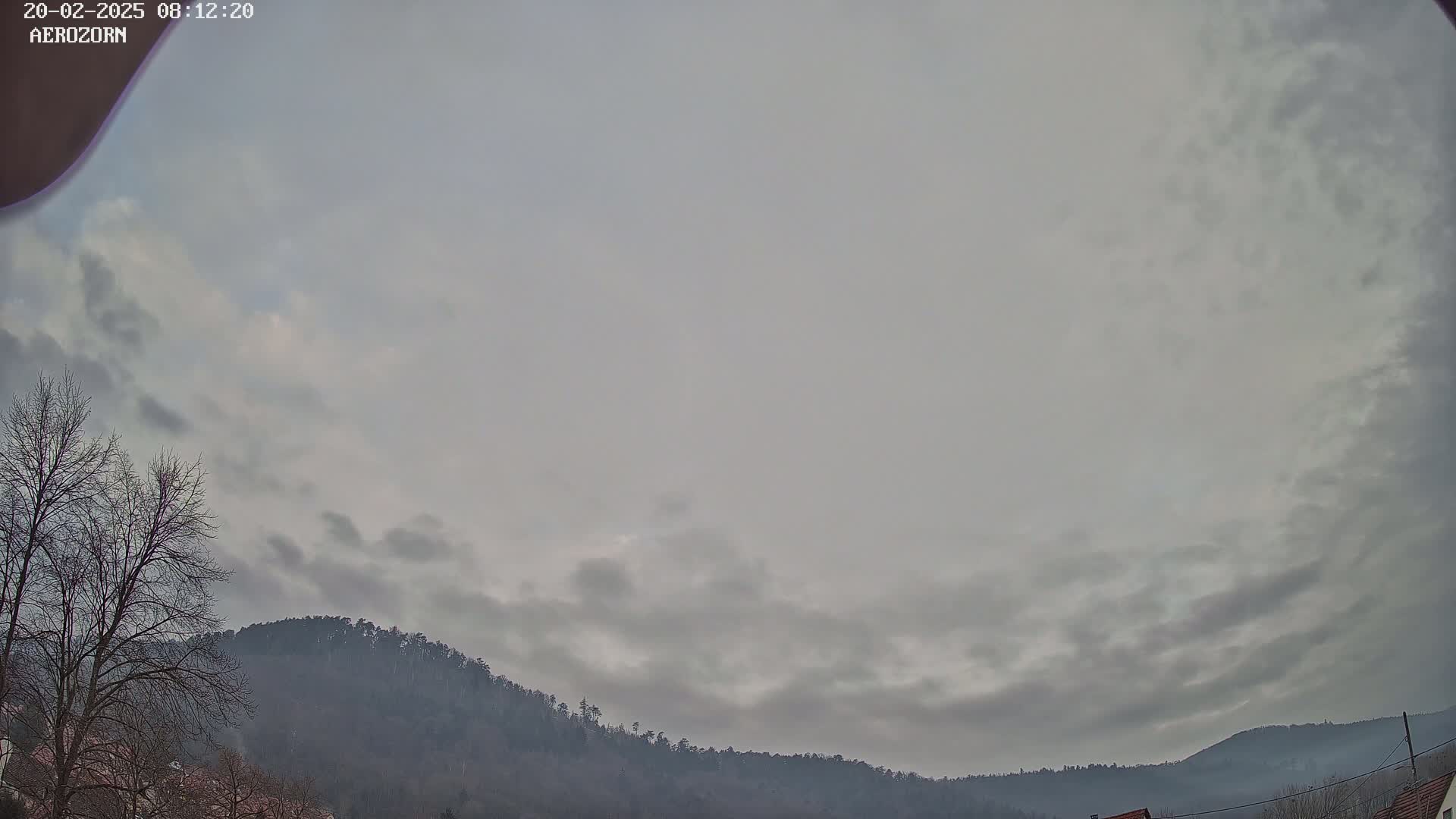 A mostly cloudy sky hangs over a line of dark, tree-covered hills.