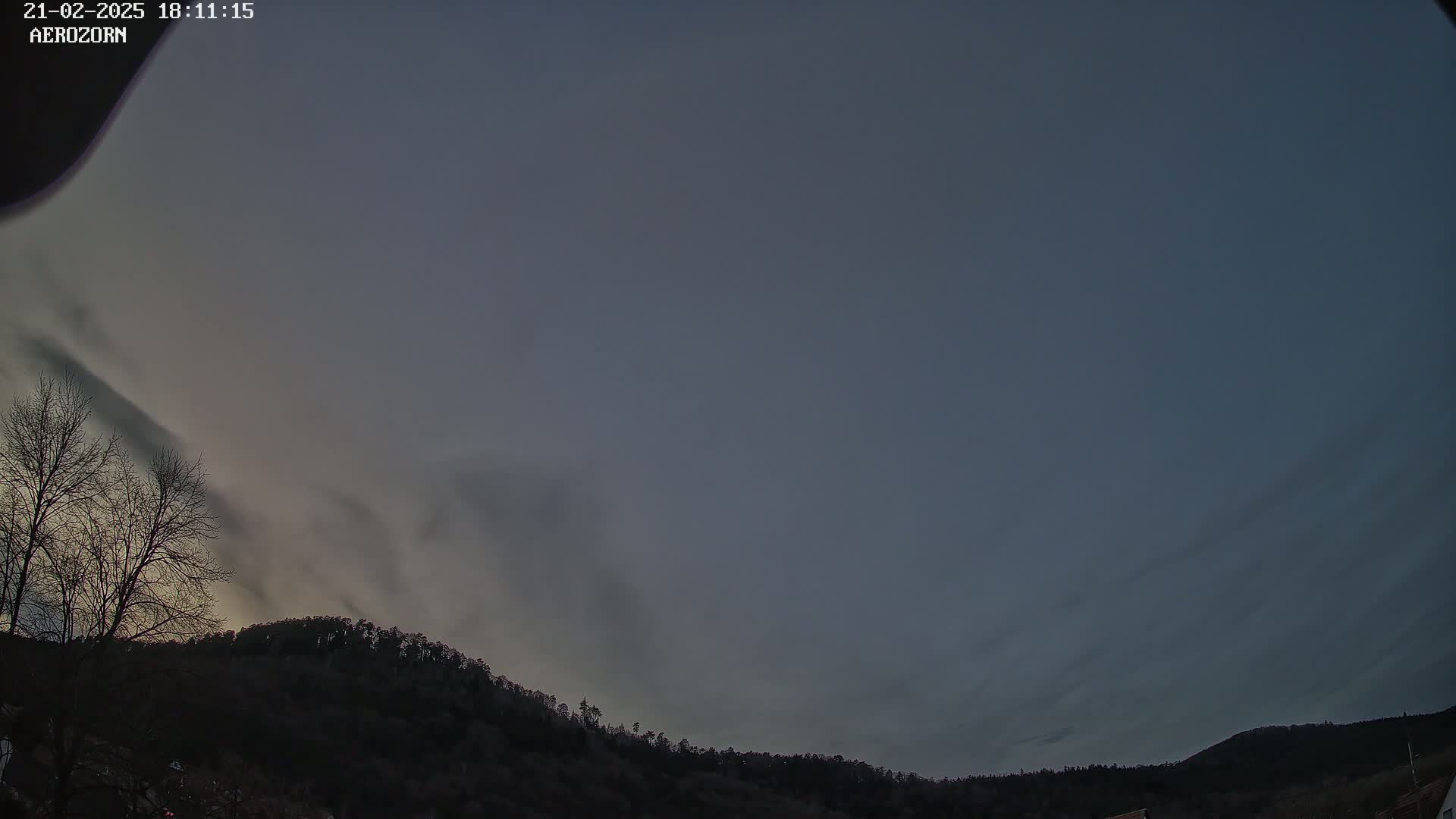 A mostly cloudy, dusky evening sky is visible above a dark, tree-covered hill.