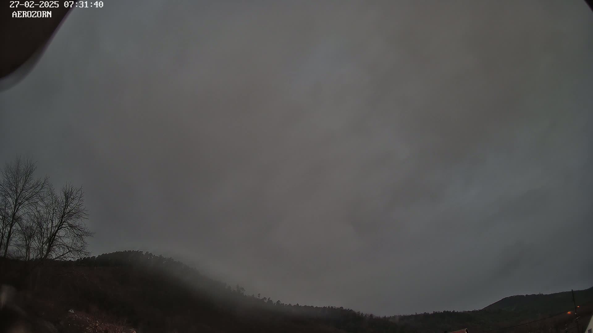 A mostly overcast sky hangs over a low, dark, forested hill under a gloomy sky.