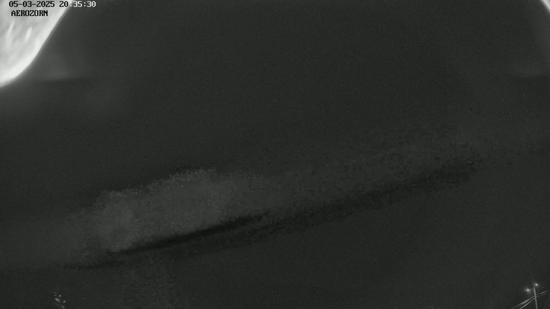 A low-light, nighttime image shows a long, horizontally oriented, blurry streak of light against a dark sky.
