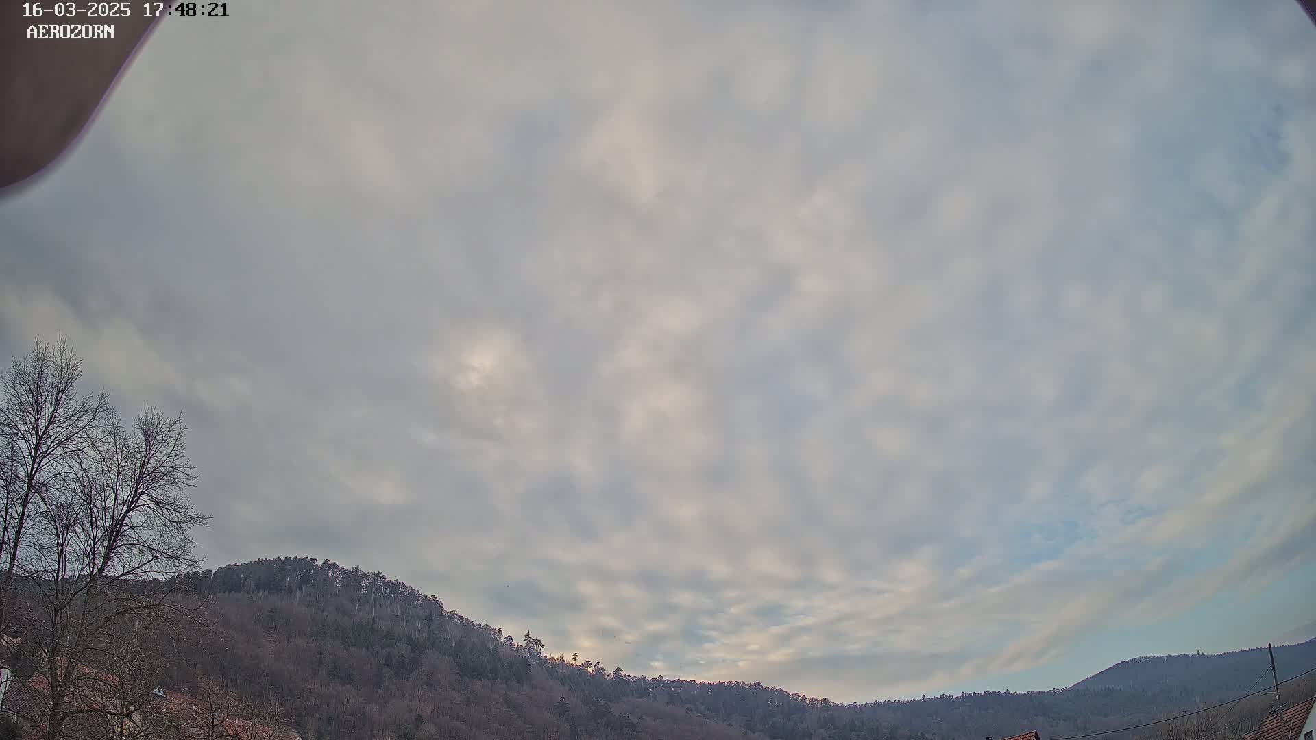 A mostly cloudy sky over a line of bare, dark-green hills.