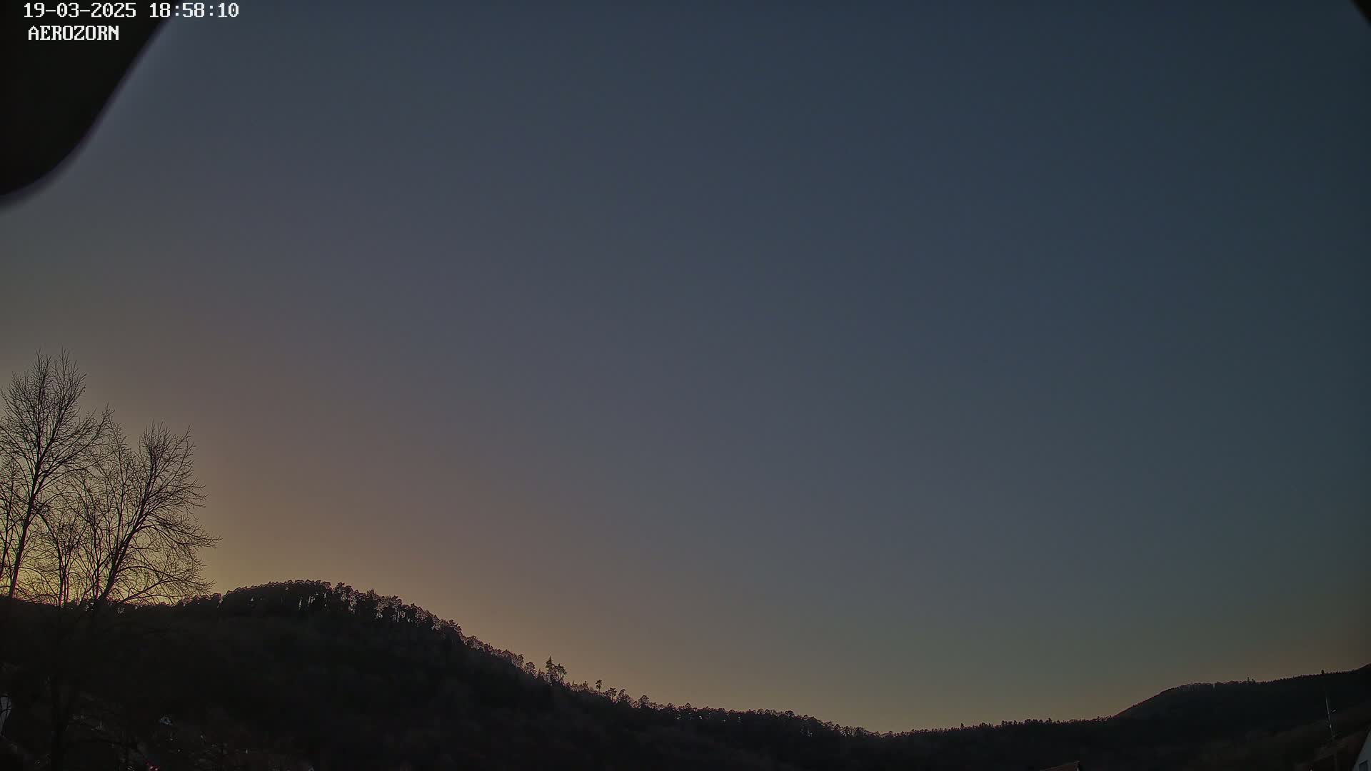 A clear, dusky twilight sky illuminates a dark, silhouetted hill covered in trees.