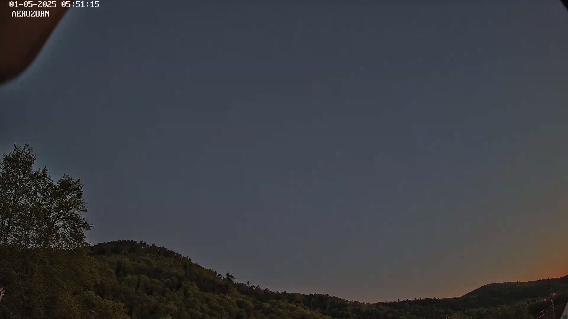 A dark, clear twilight sky is visible above a line of dark green, tree-covered hills.