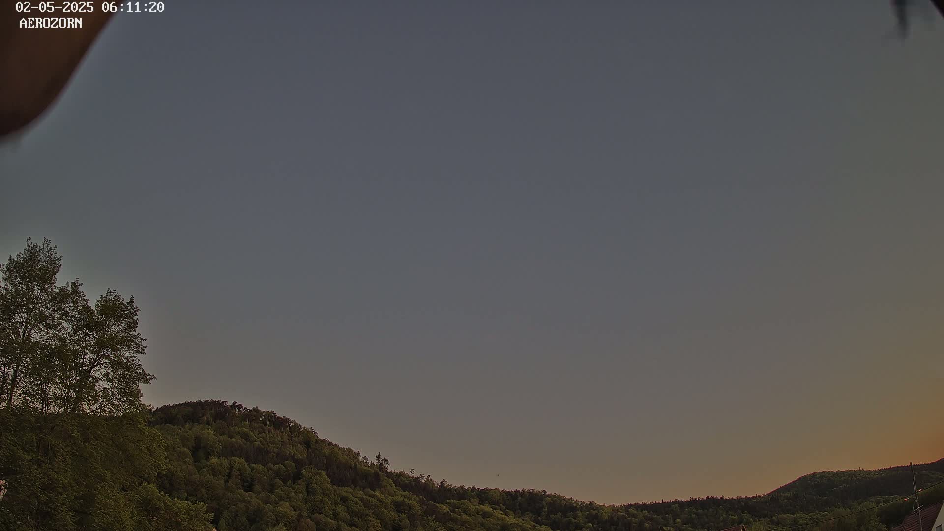 A mostly clear, dusky sky is visible above a line of dark green, tree-covered hills.