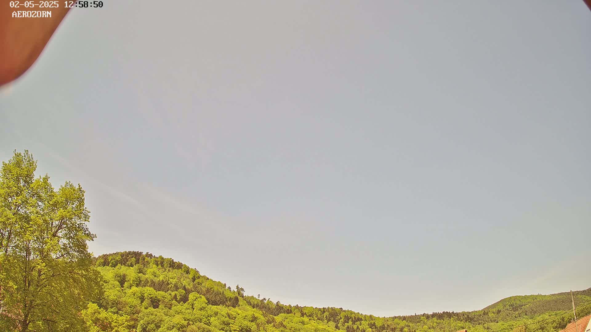 A mostly clear sky overlooks a gently curved line of lush, green hills and trees.