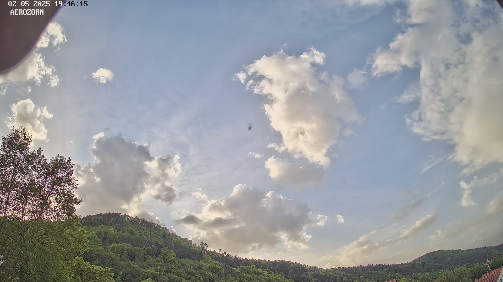Partly cloudy skies over a lush green hill, visible under a mostly clear blue sky.