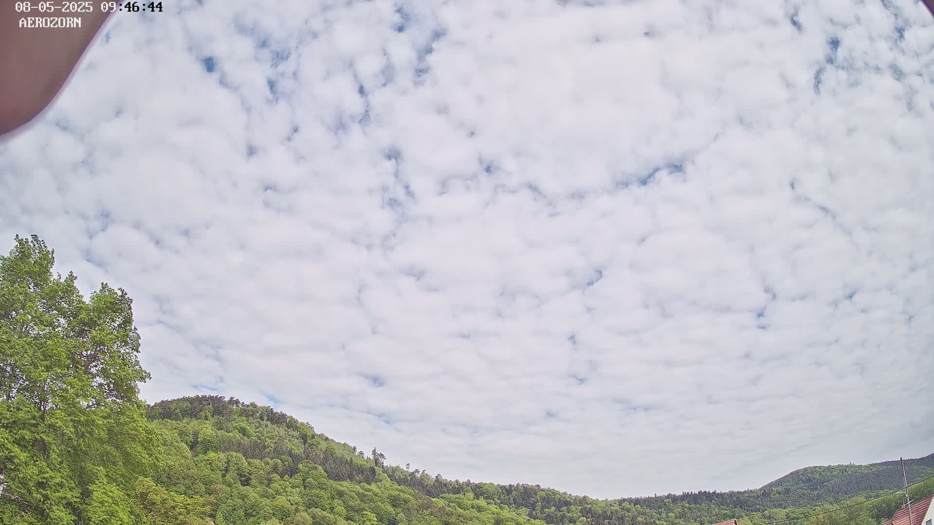 A mostly cloudy sky is visible above a lush green hillside.