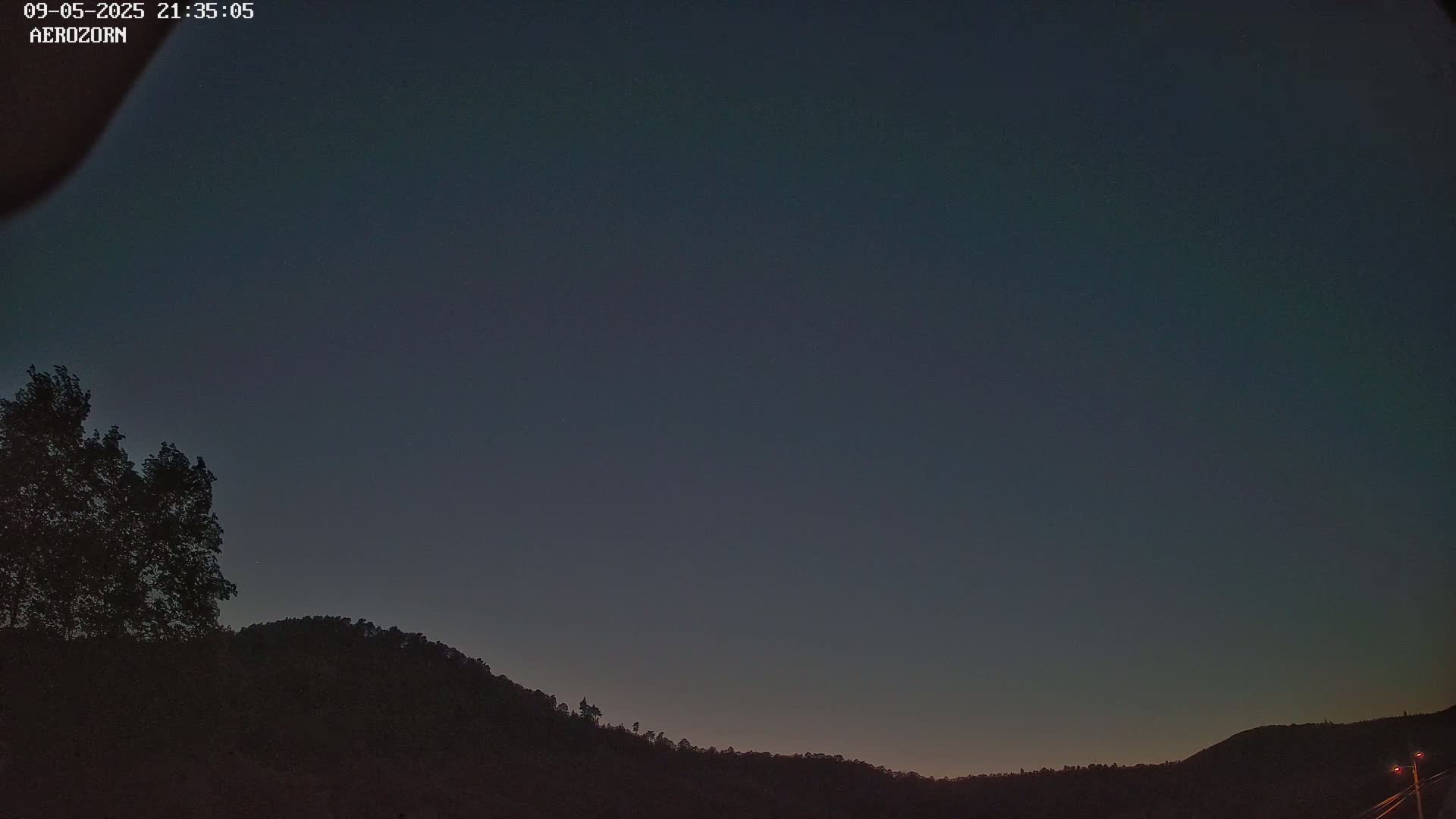 A dark, clear night sky is visible above a silhouetted line of trees and hills.