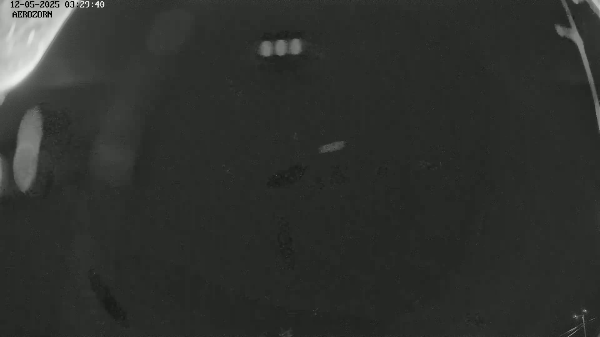 A dark grayscale image shows a blurry, mostly dark area with a few lighter, indistinct shapes and spots of varying brightness.