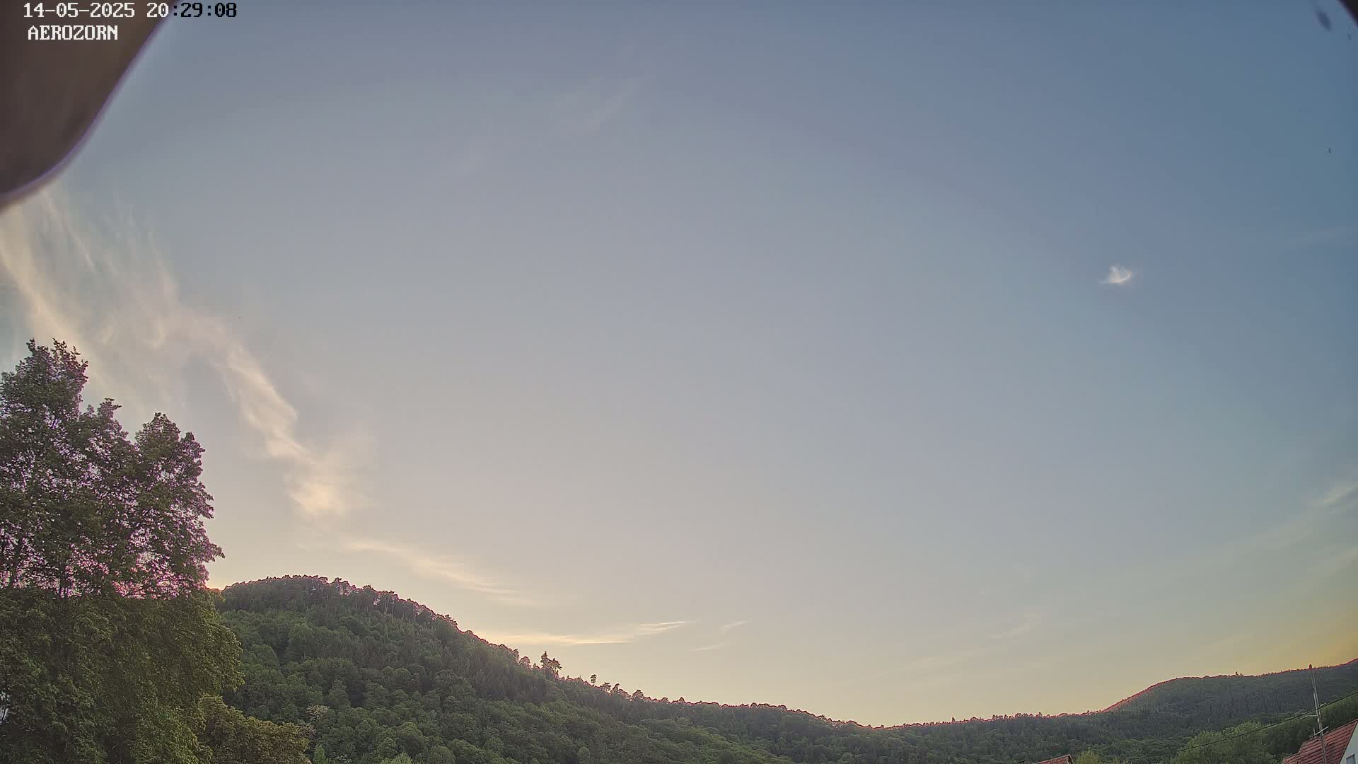 A mostly clear, twilight sky is over a tree-covered hill.