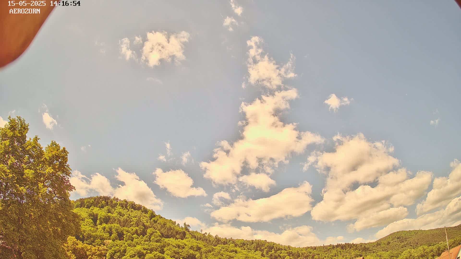 A partly cloudy sky is visible above a lush green hill covered in trees.
