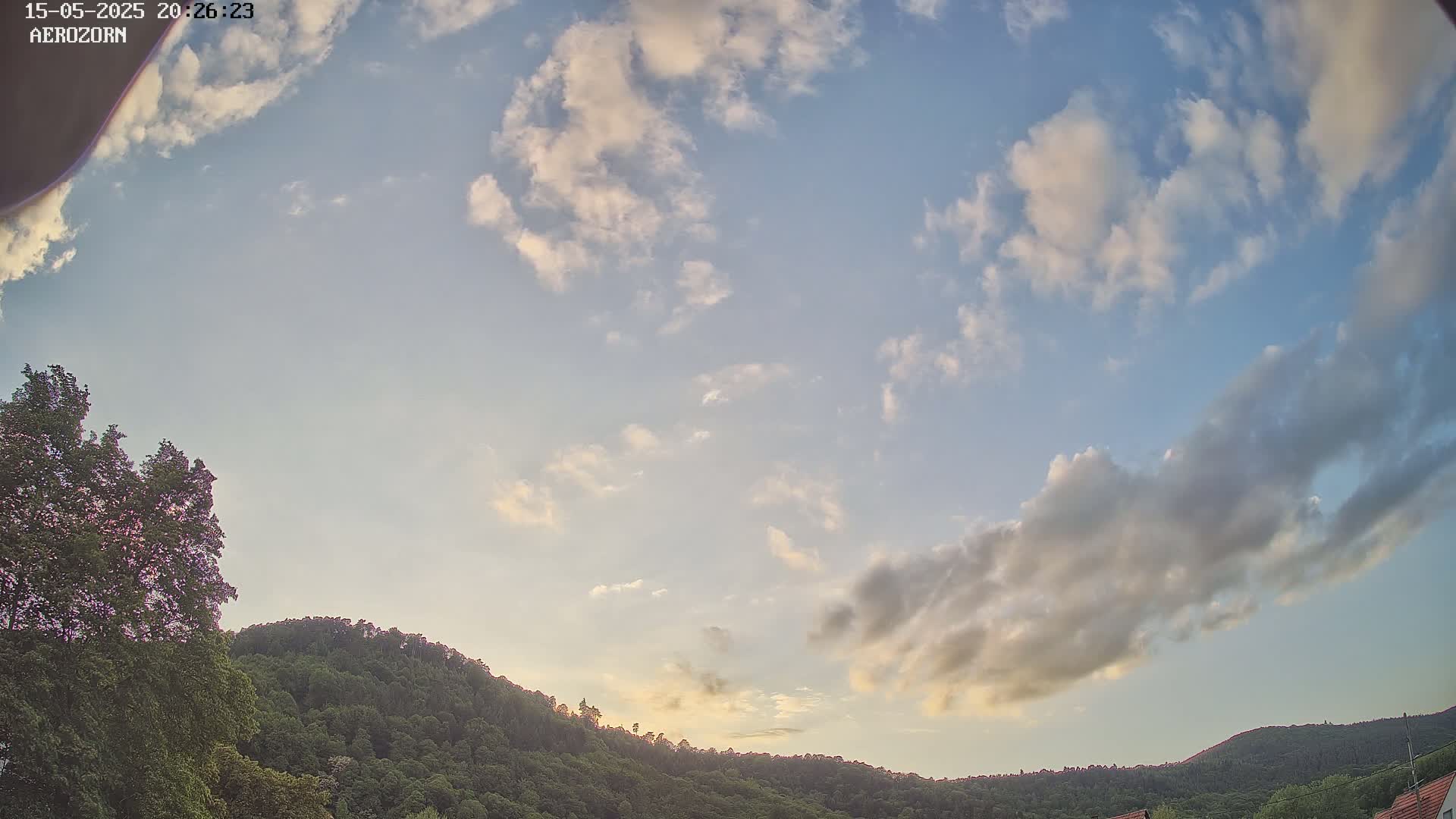 A partly cloudy evening sky overlooks a line of forested hills.