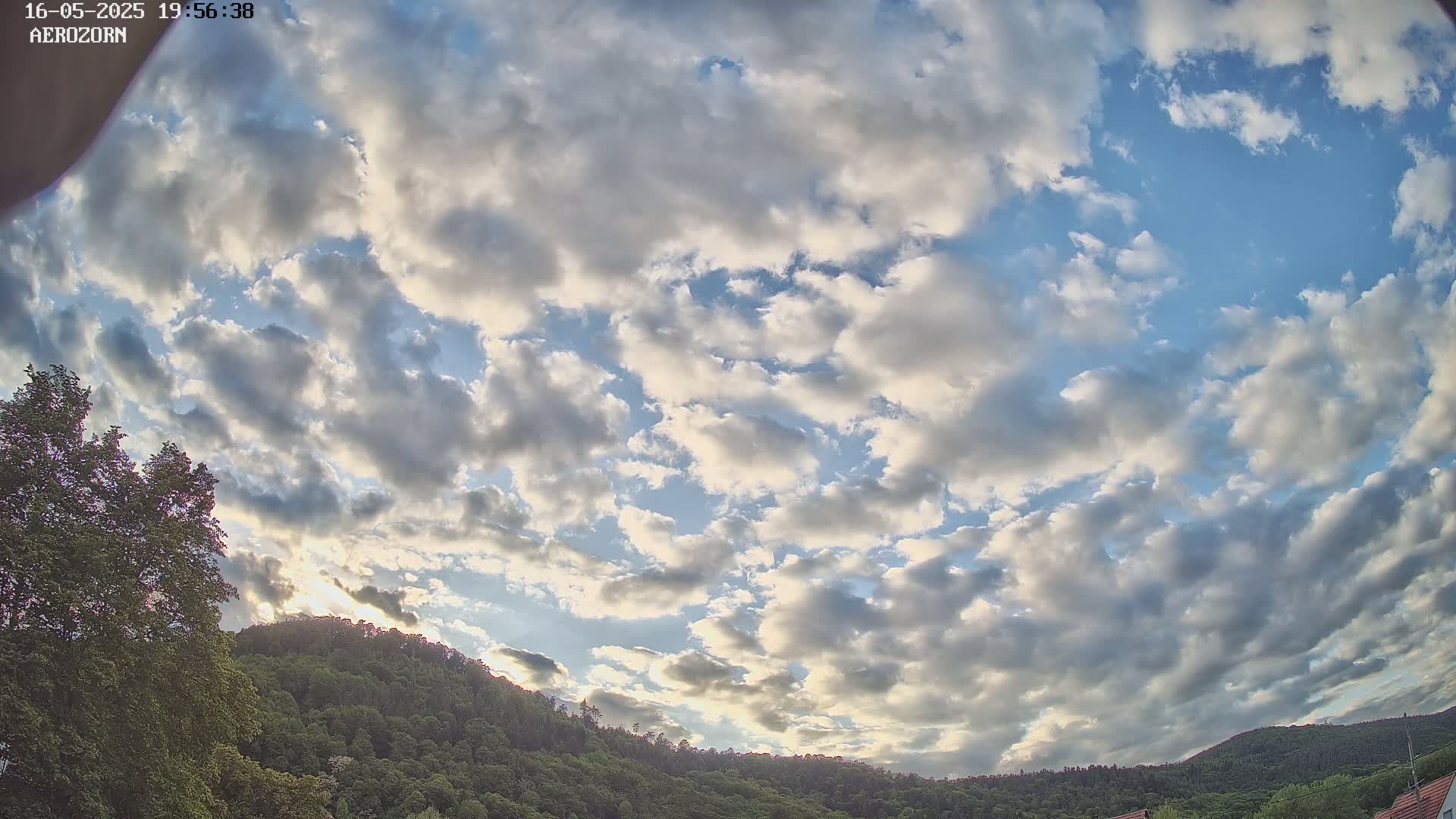 A partly cloudy sky with numerous scattered cumulus clouds over a lush green, hilly landscape.
