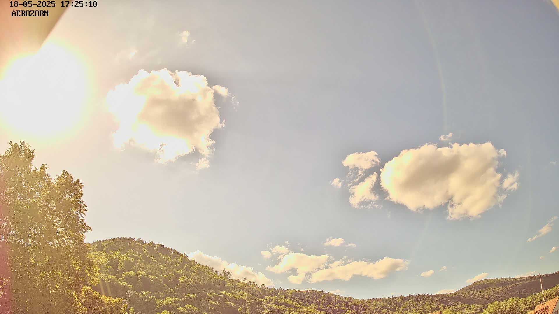 A mostly sunny sky with fluffy white clouds floats above a lush green hillside.