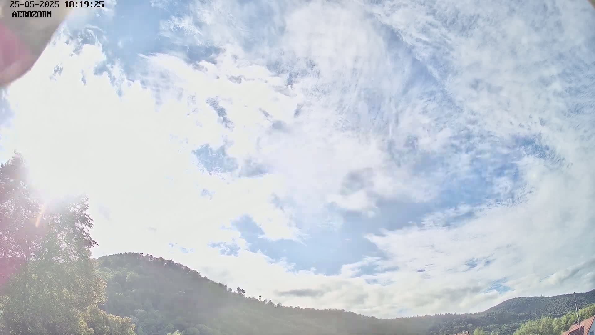 A mostly sunny sky with scattered clouds is visible above a line of green hills.