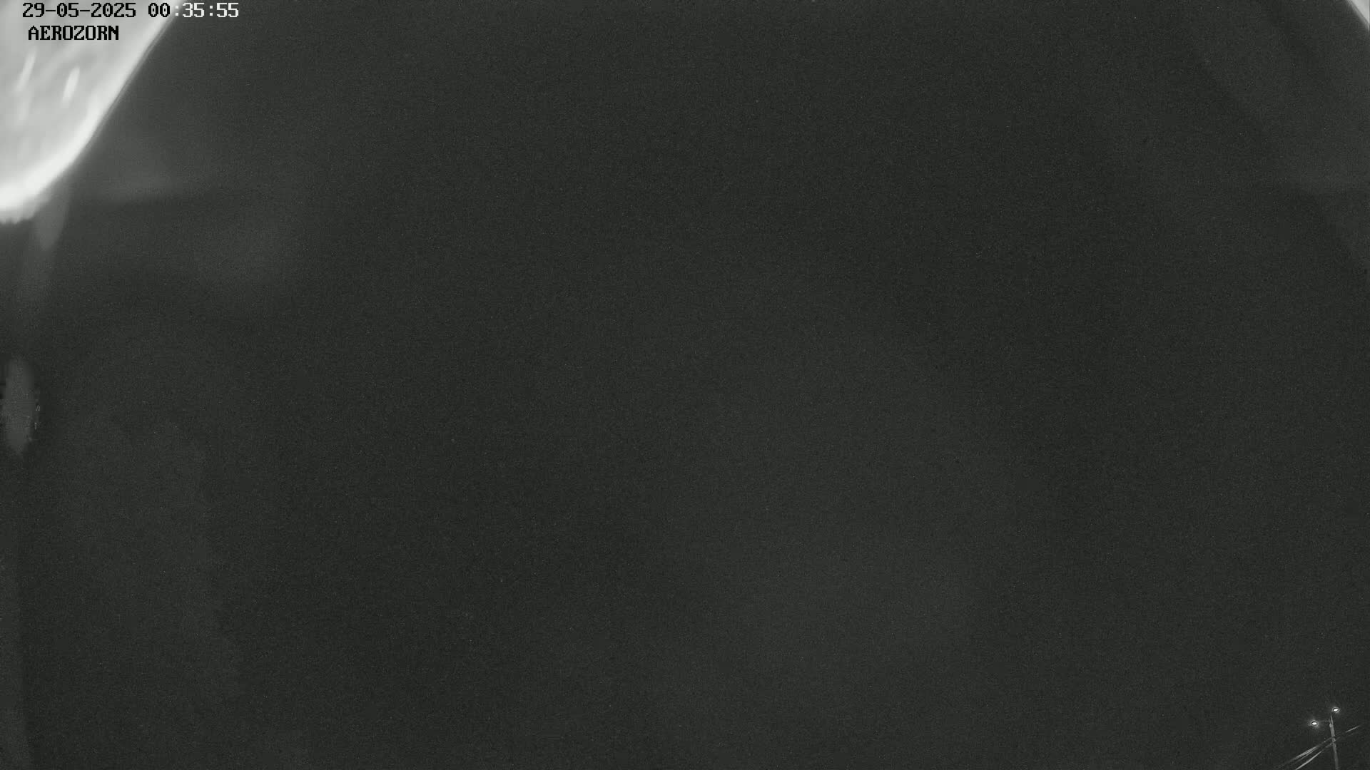 A nighttime, grainy image shows a dark sky with a faint, blurry light source in the upper left corner.