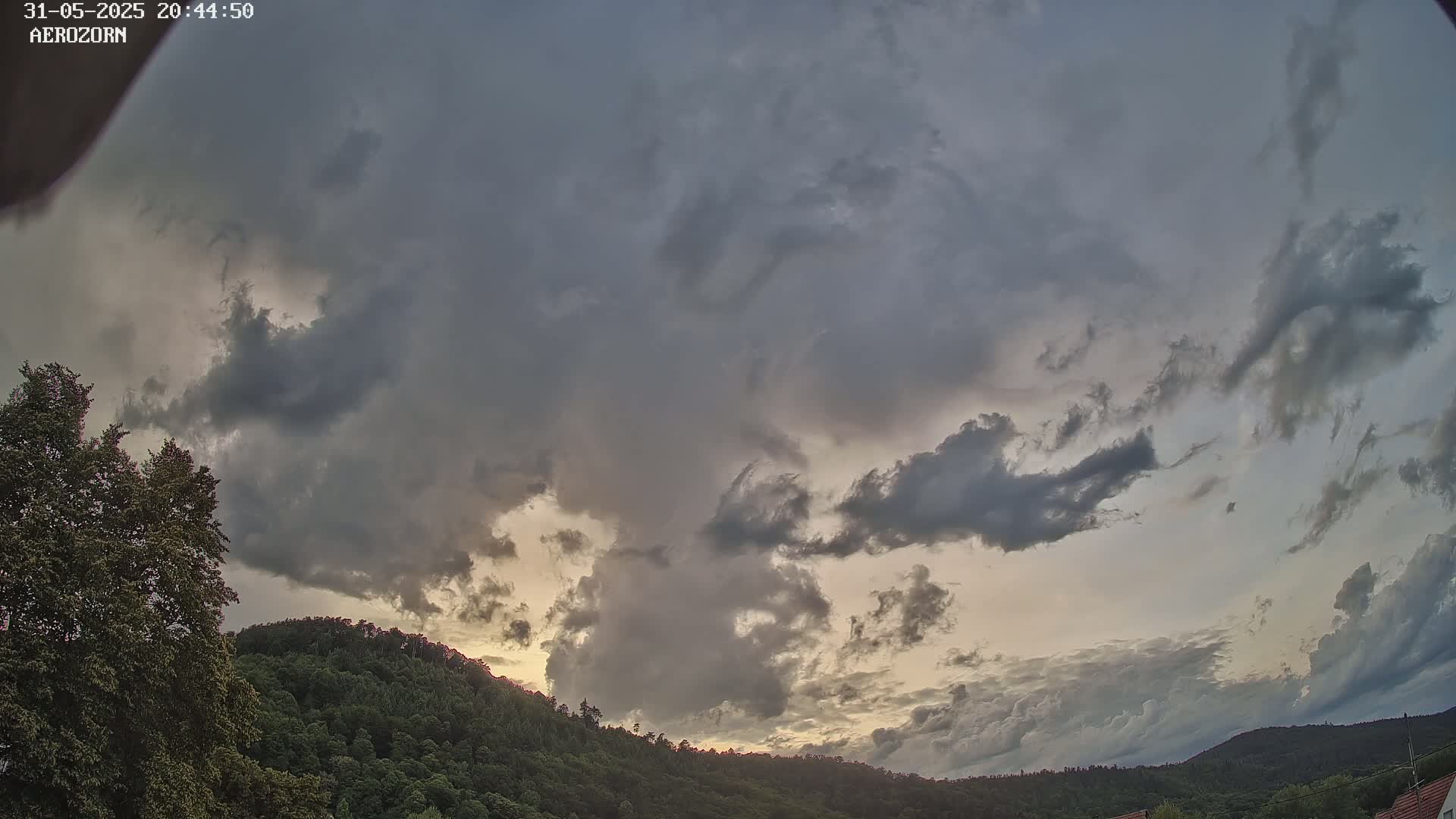 Overcast skies with dark, swirling clouds above a line of green hills at sunset.