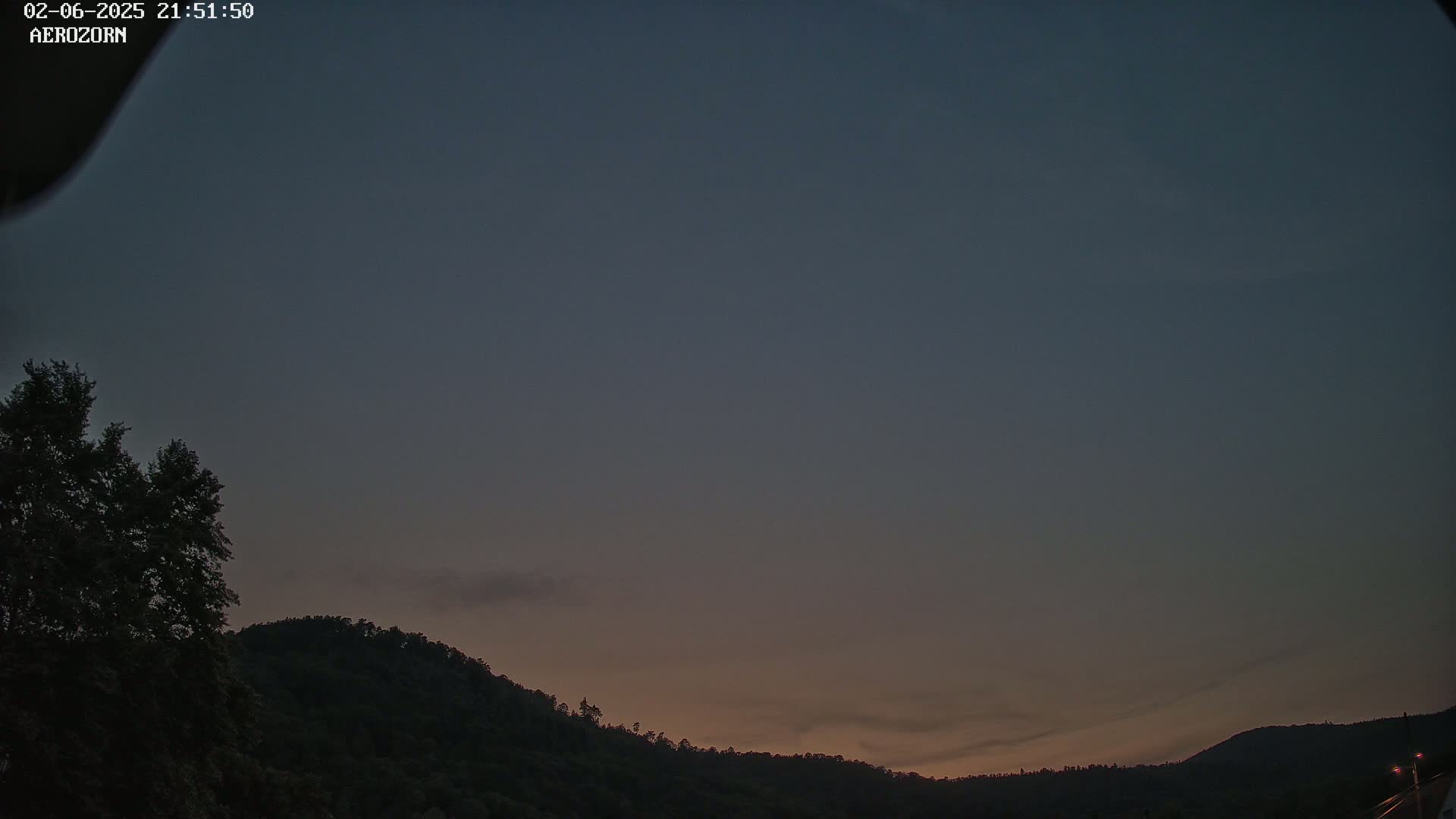 A dark, mostly clear twilight sky hangs over a silhouetted line of hills and trees.