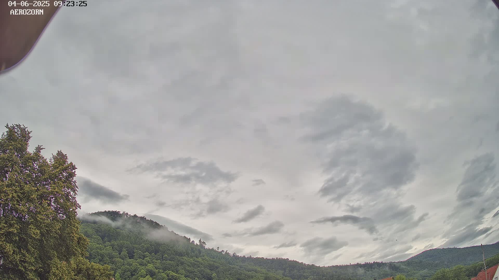 A mostly cloudy sky hangs over a line of forested hills partially shrouded in fog.