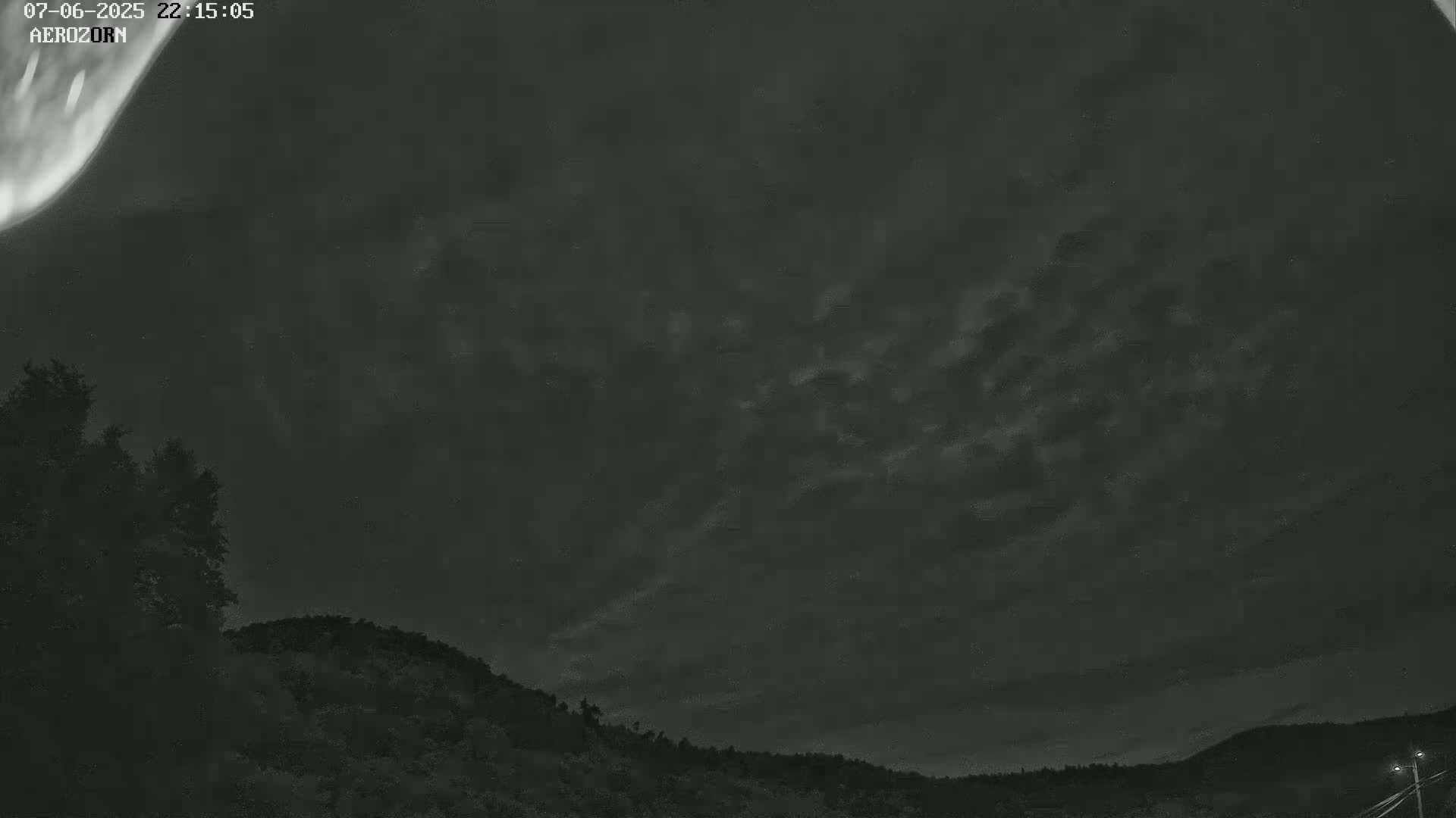 A nighttime, cloudy sky with a faint aurora borealis is visible above a dark, silhouetted landscape of trees and hills.