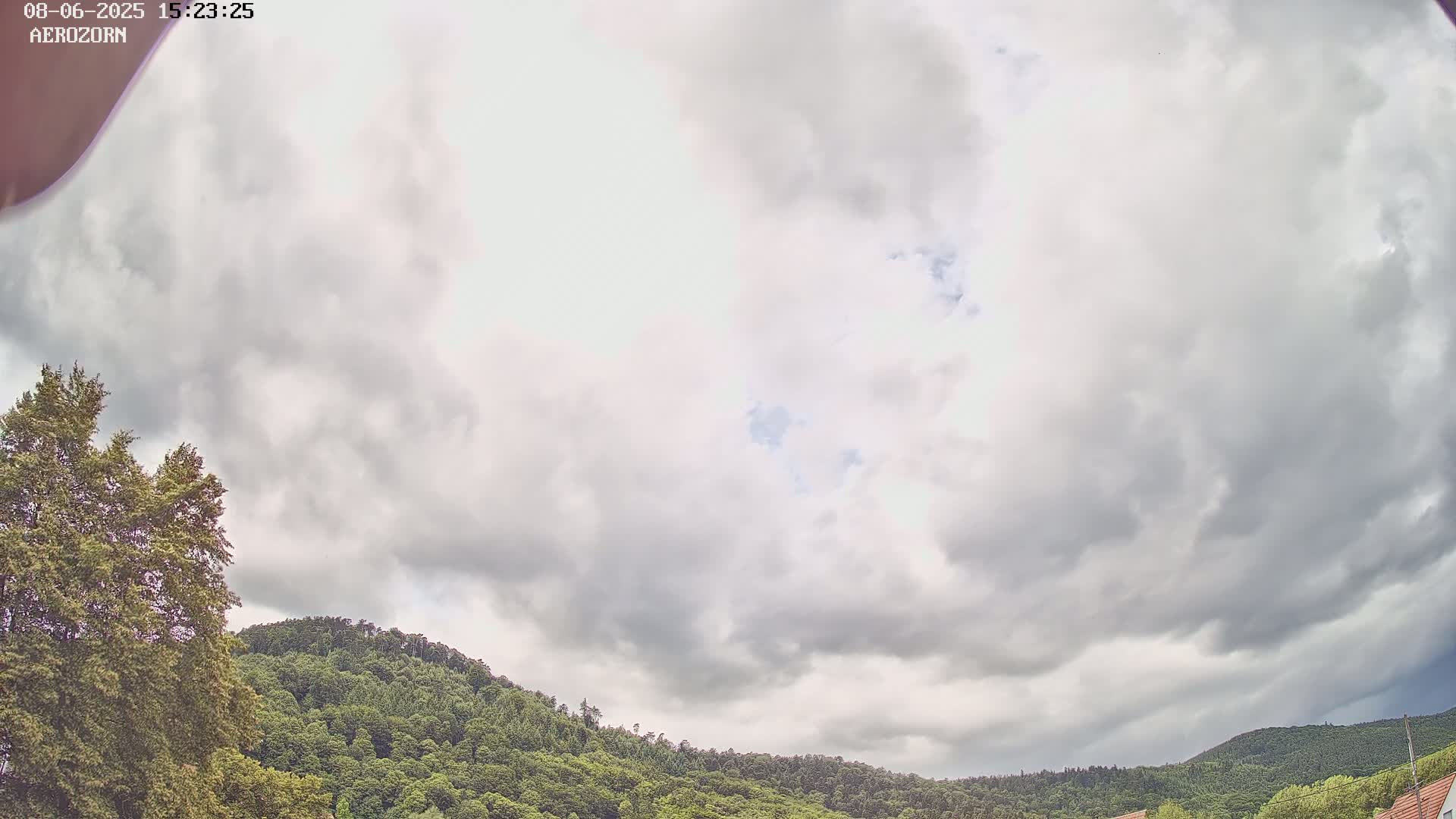 A mostly cloudy sky hangs over a lush, green, tree-covered hillside.