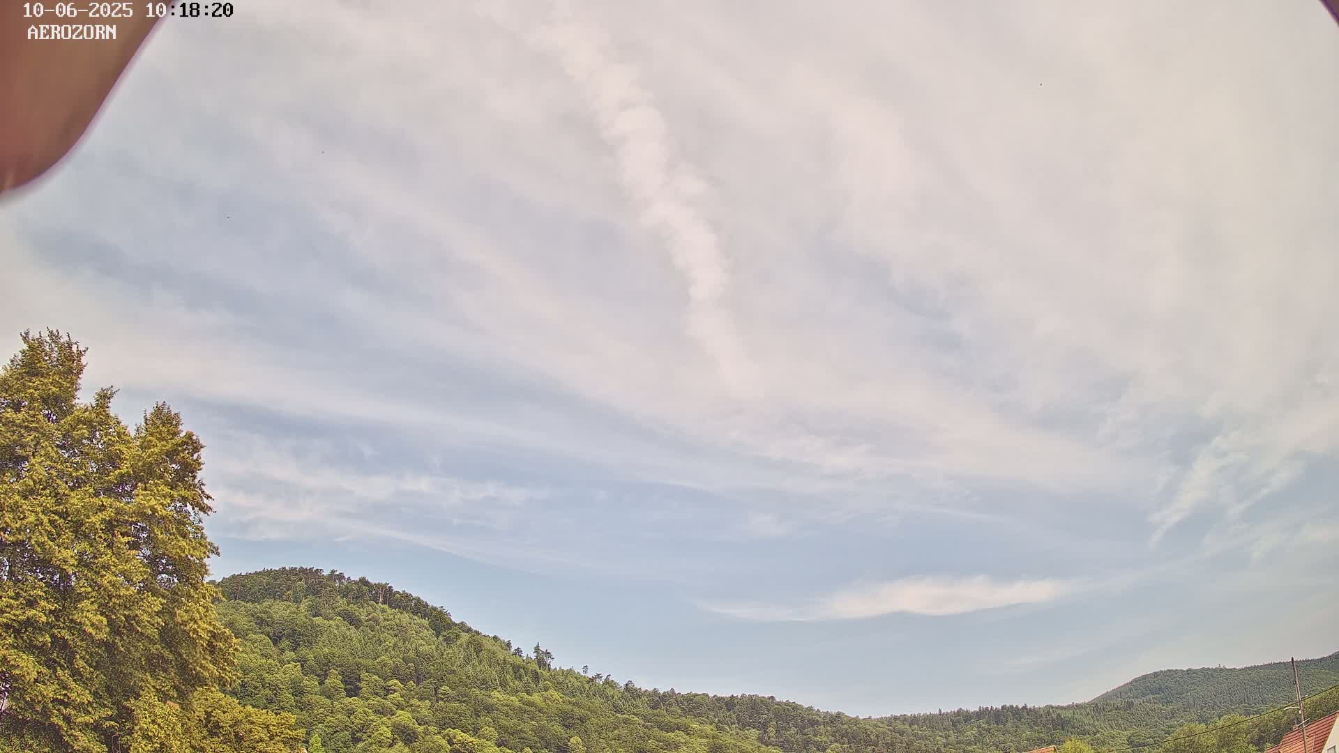 A mostly cloudy sky with wispy clouds hangs over a lush green hill covered in trees.