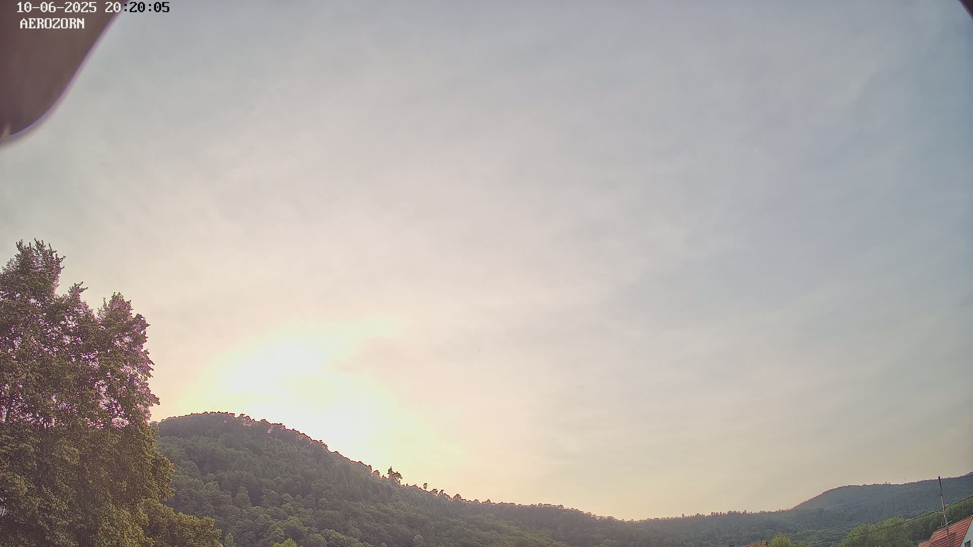 A mostly clear, pale sky with a soft light illuminating tree-covered hills.