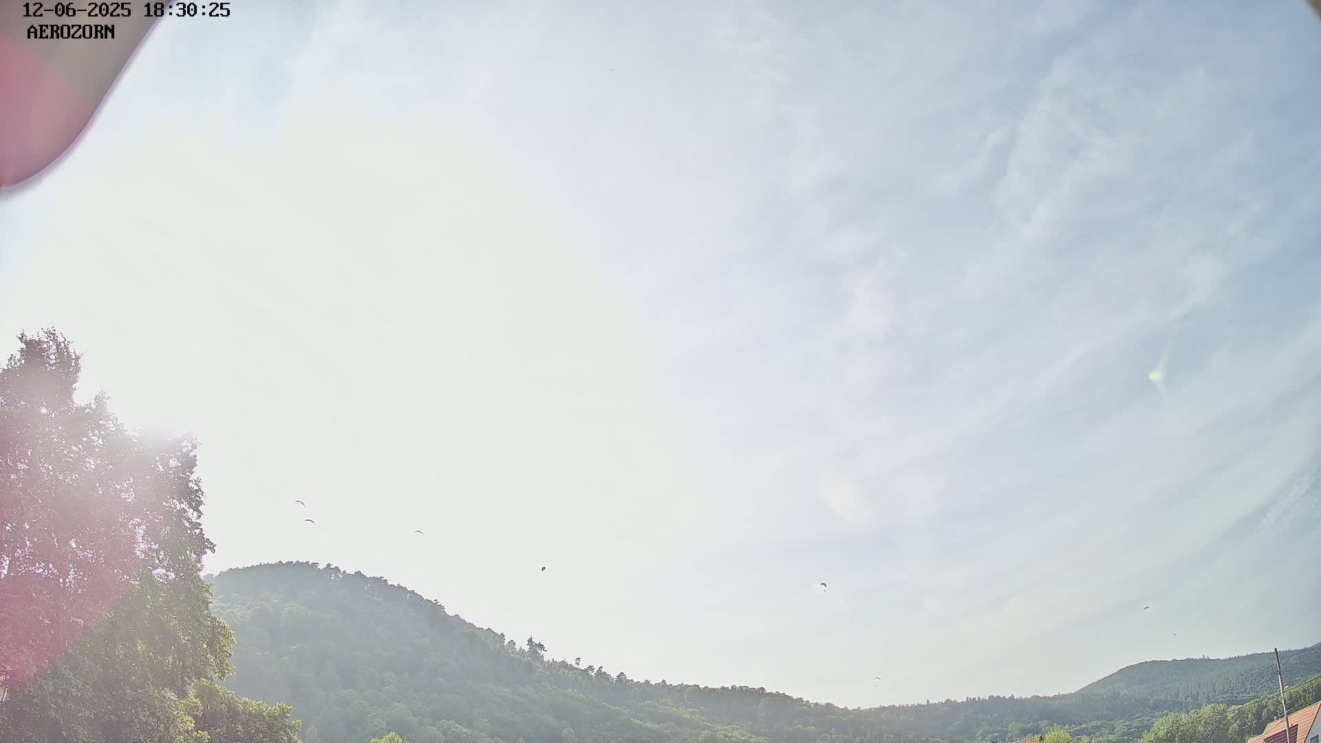 Several paragliders fly in a partly cloudy sky above a line of green hills.