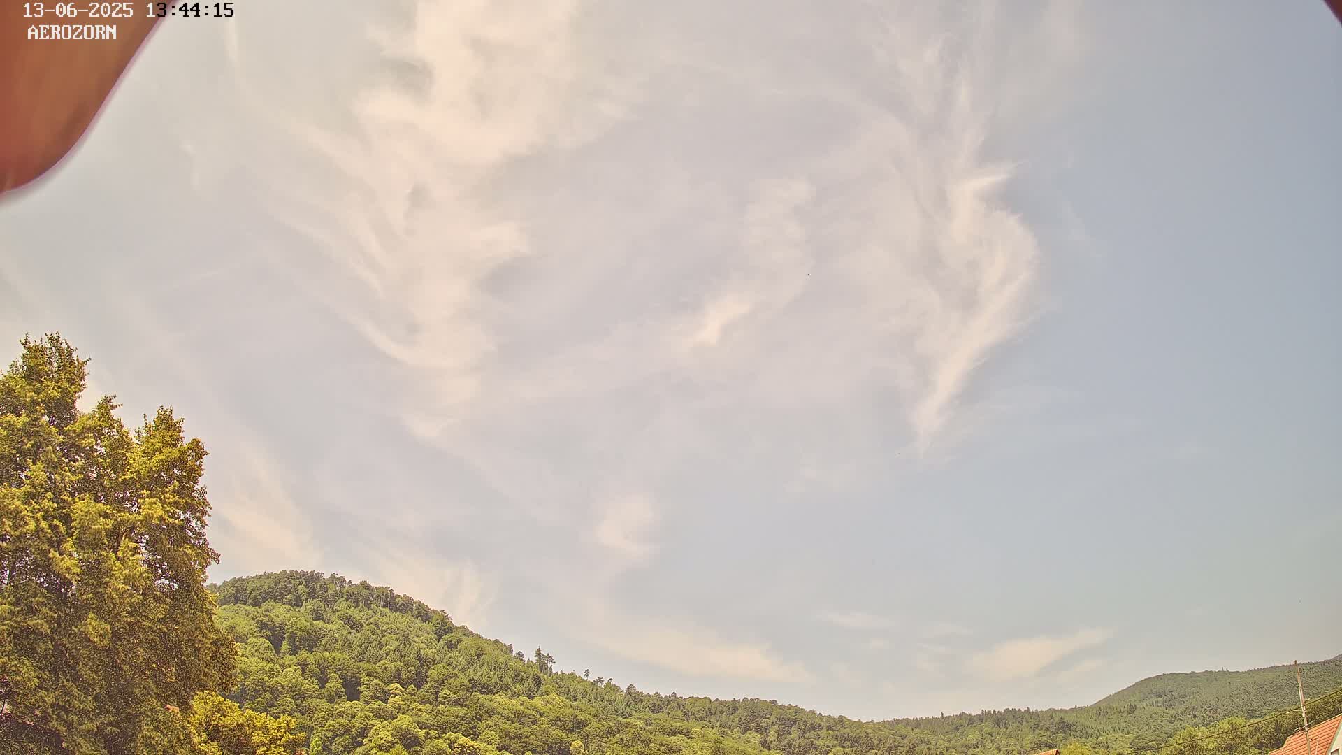 A mostly clear sky with wispy clouds above a line of green, tree-covered hills.