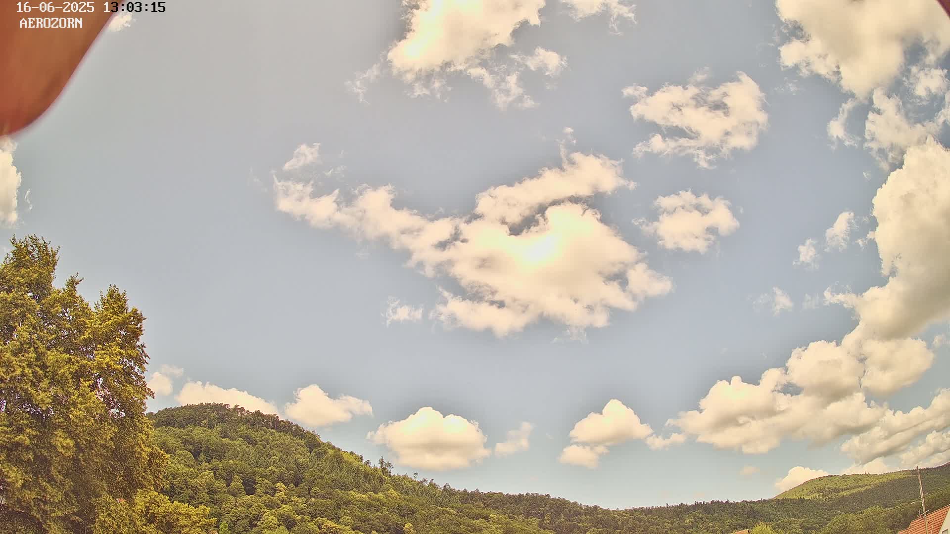 A partly cloudy sky with fluffy white clouds is visible above a line of green hills and trees.
