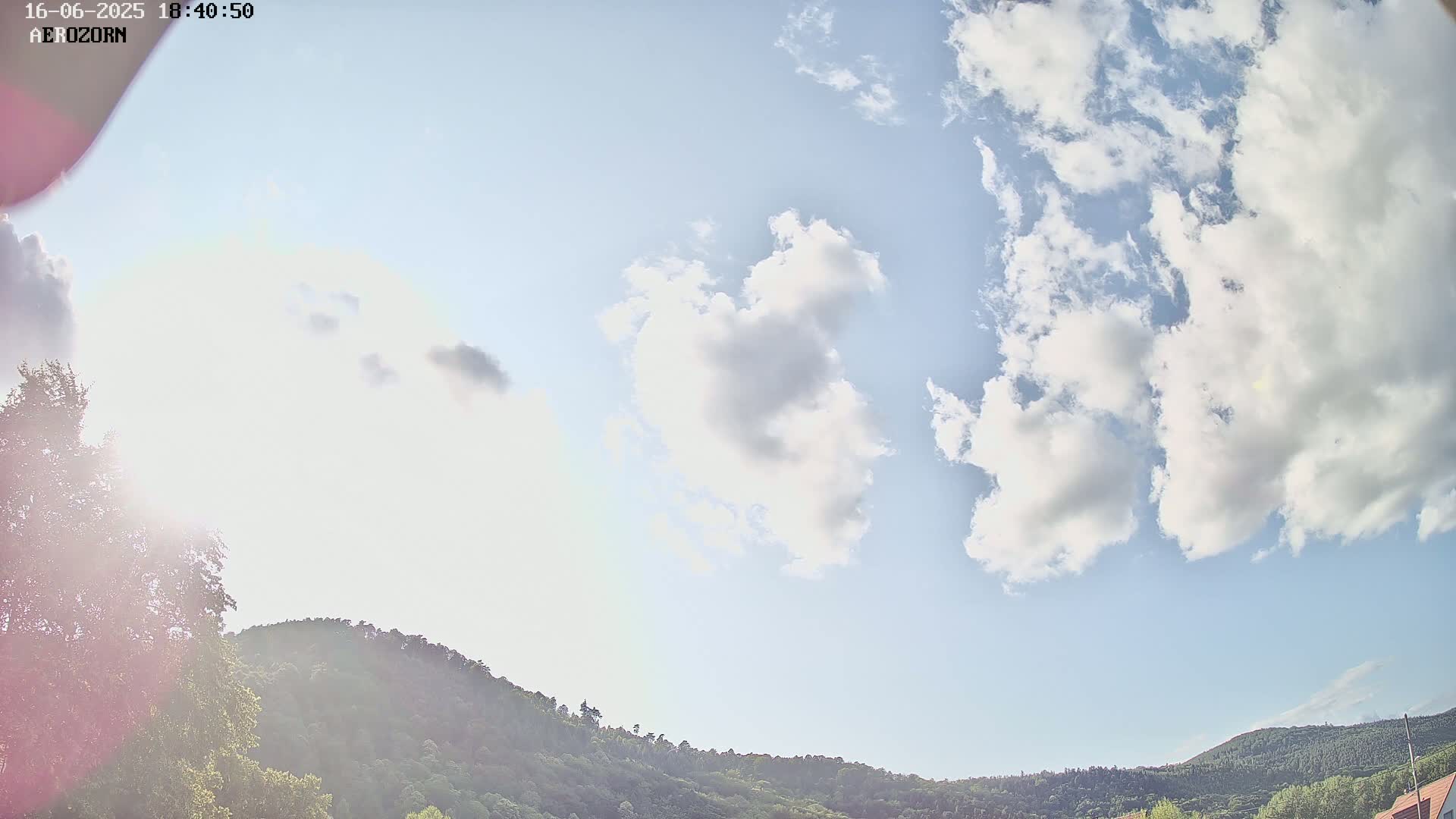 A partly cloudy sky with fluffy white clouds is visible above a line of green hills under a bright sun.
