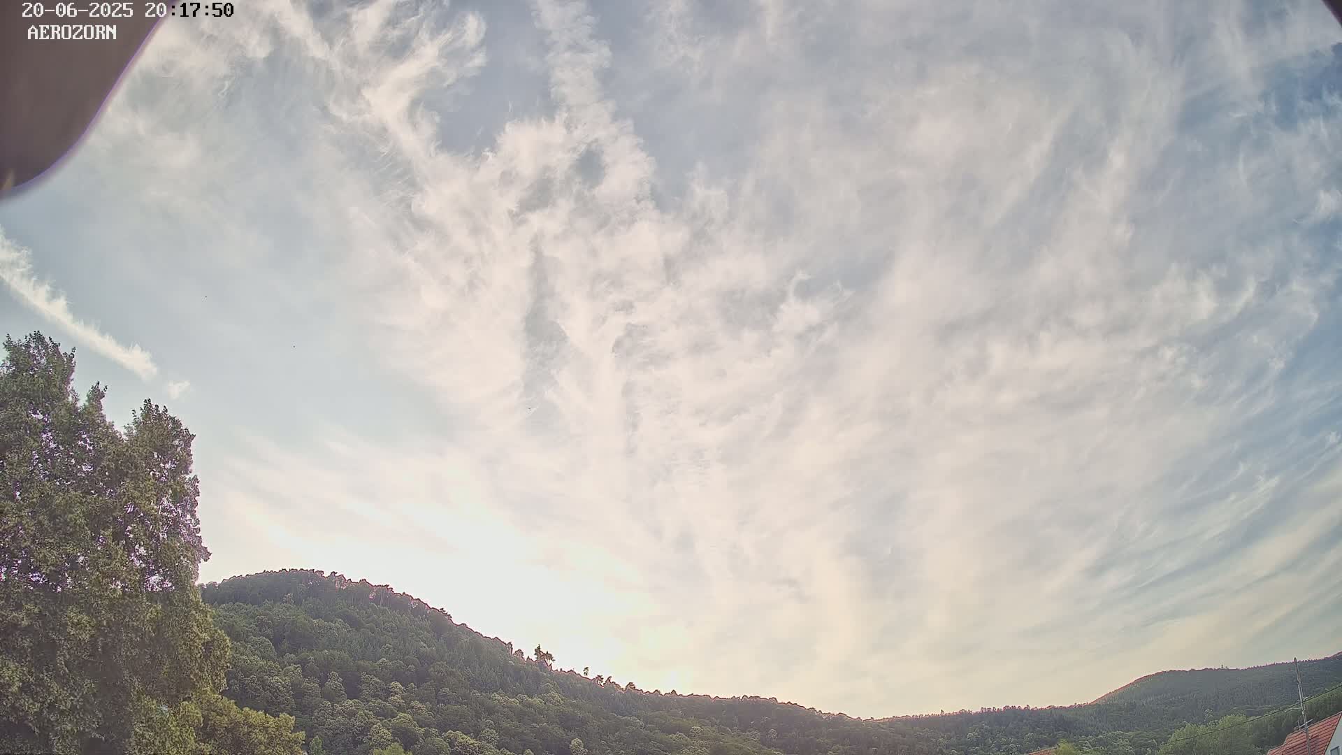 A mostly cloudy sky, with wispy clouds, overlooks a gently curving line of green hills and trees.