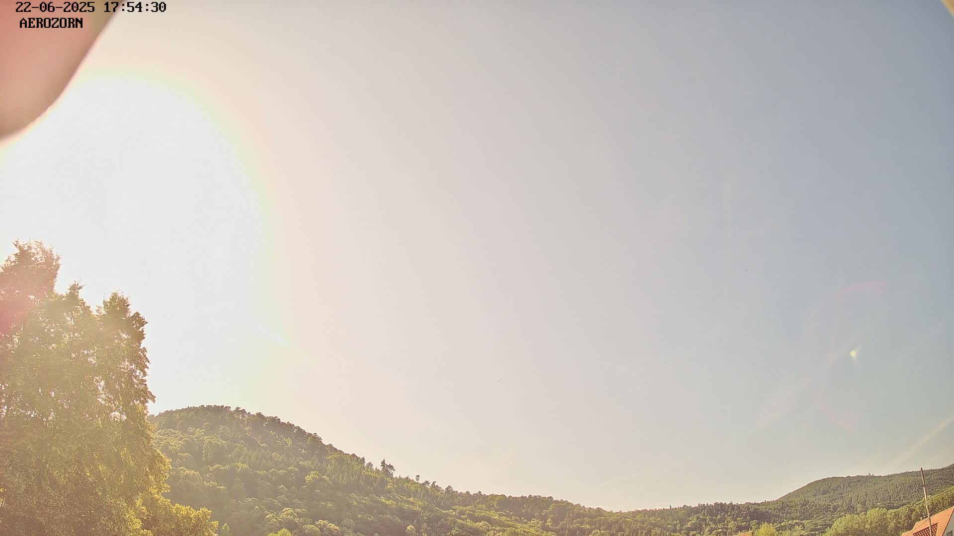 A bright, mostly clear sky is visible above a line of lush green hills and trees.