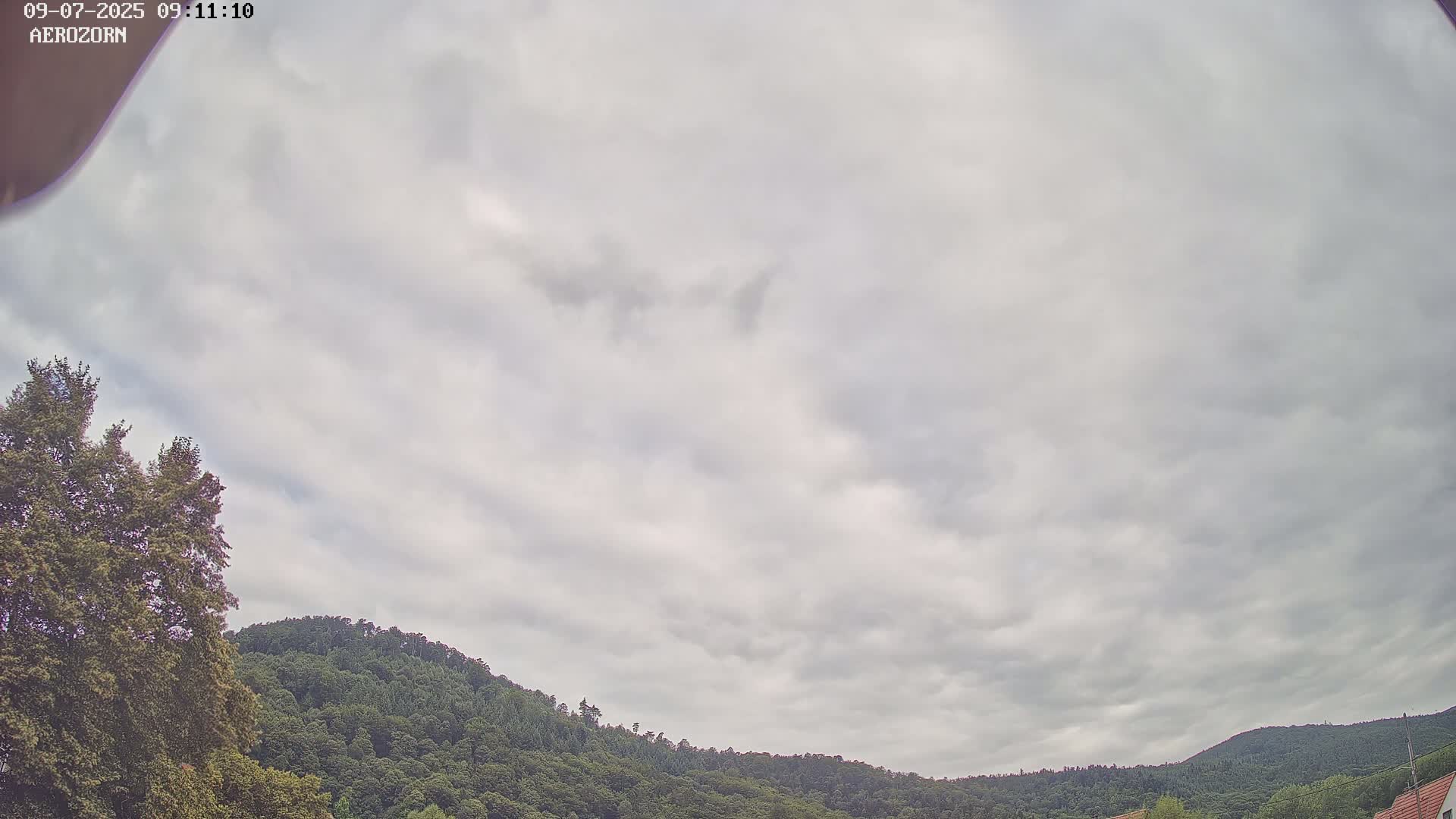 A mostly cloudy sky overlooks a tree-covered hillside.