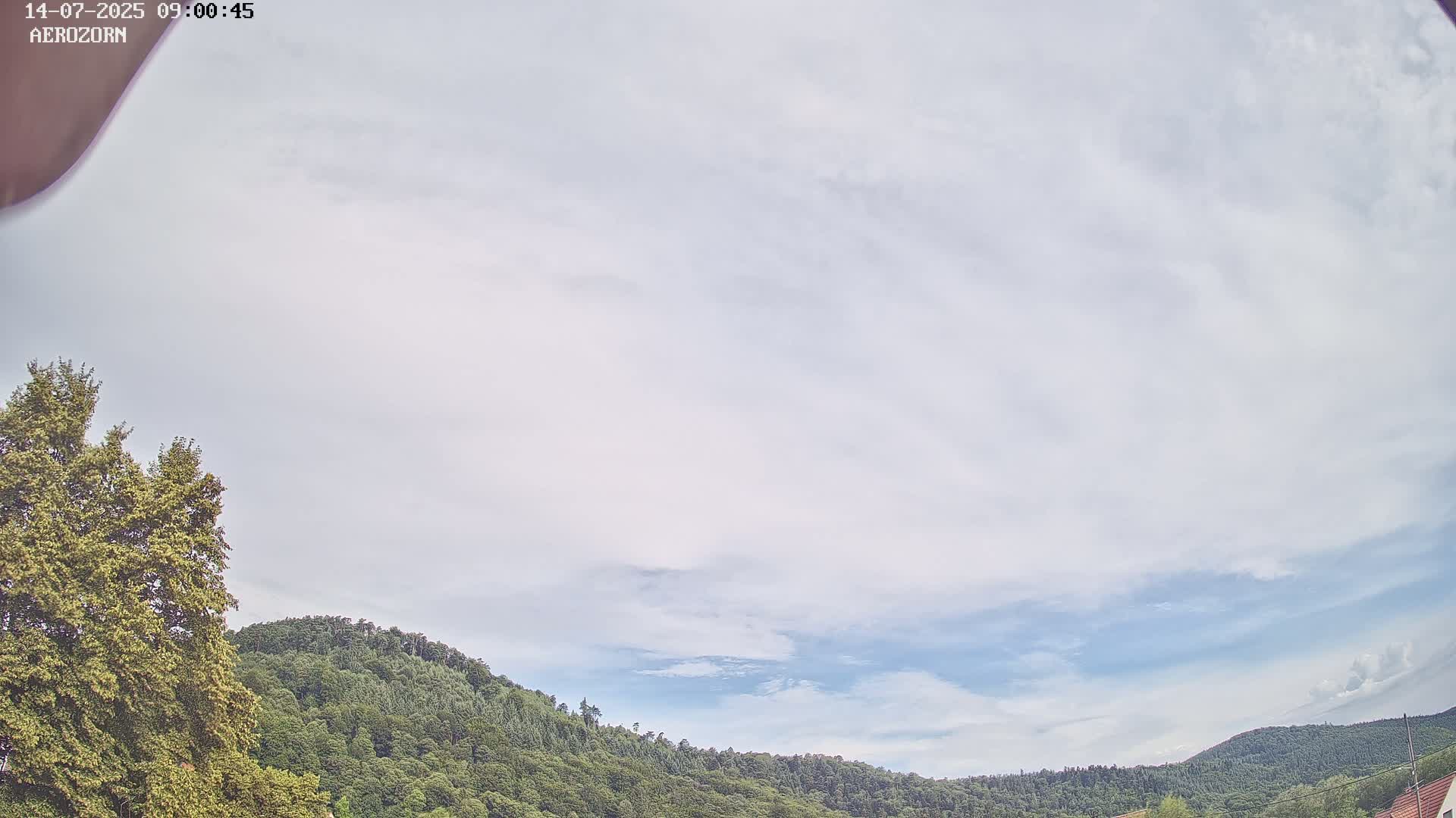 A mostly cloudy sky overlooks a line of green, tree-covered hills.