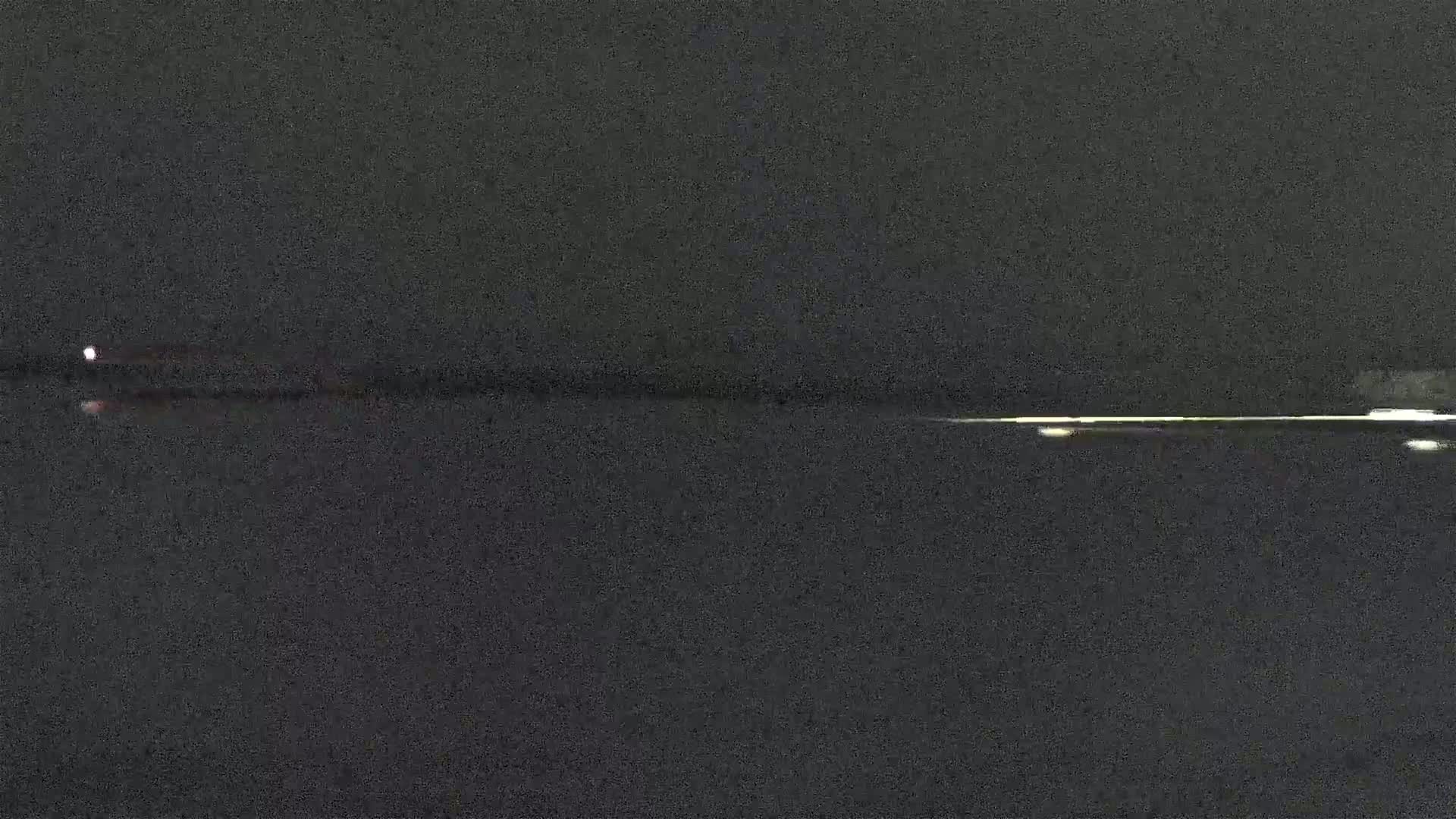 A dark body of water reflects a faint light source at night under a dark sky.