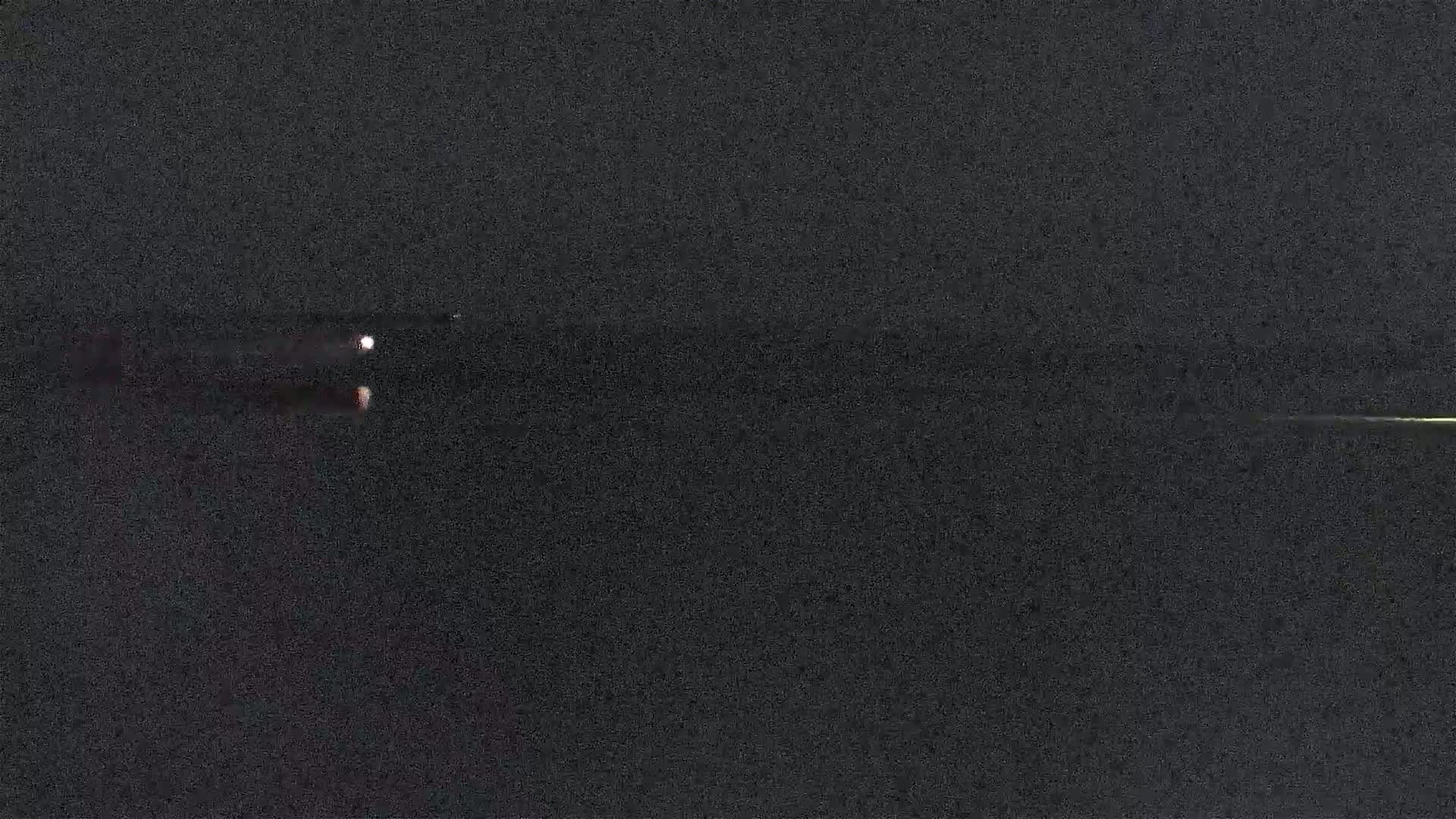 At night, two faint lights appear on a dark body of water with a faint light on the horizon.
