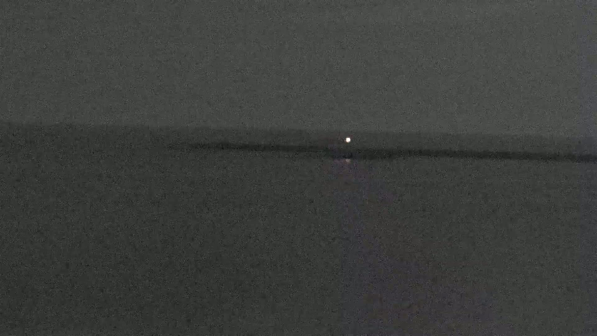 A small, bright light is visible on a dark body of water under a dark sky.