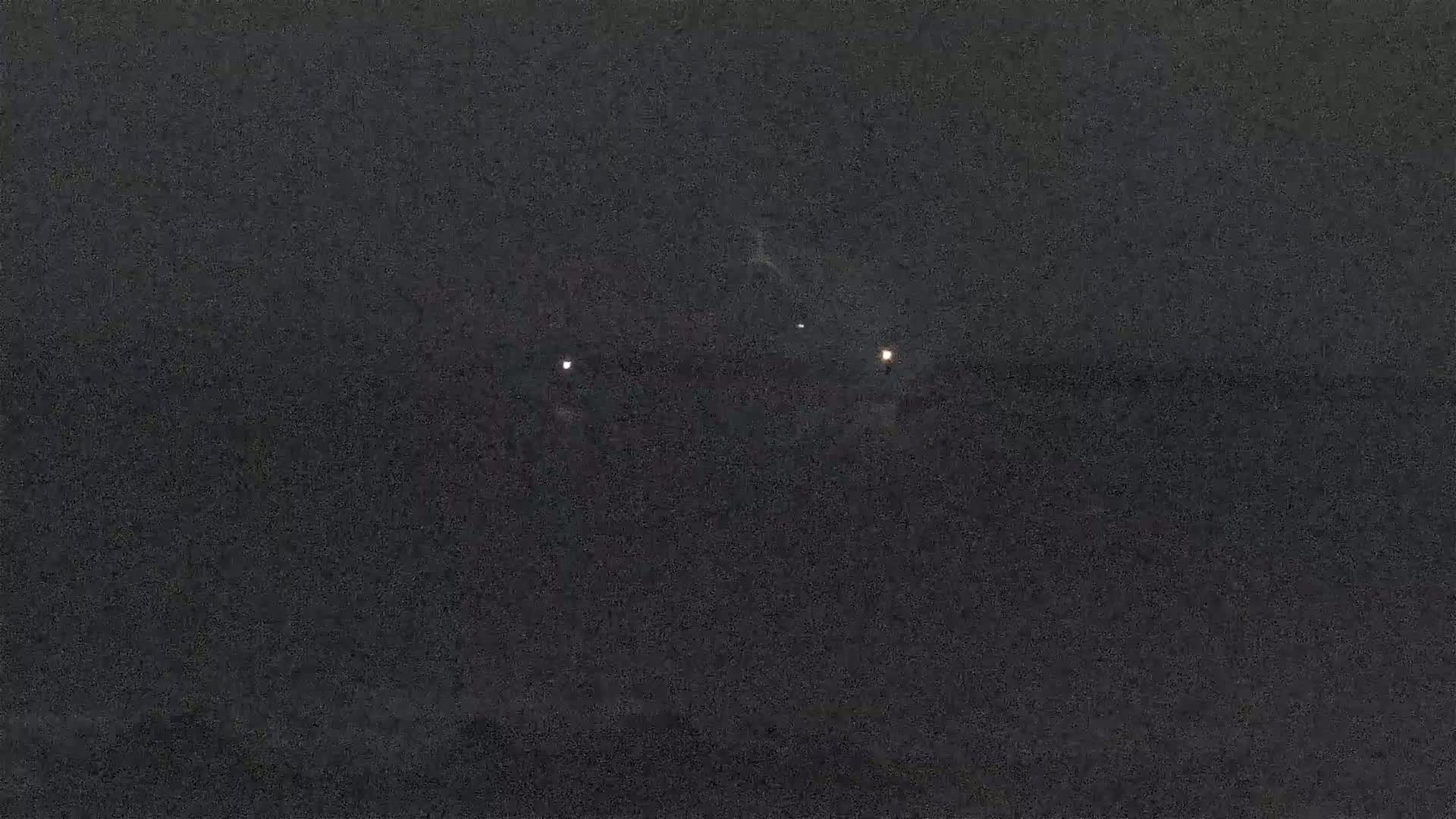 A dimly lit, dark scene at night shows a few small lights in the distance.